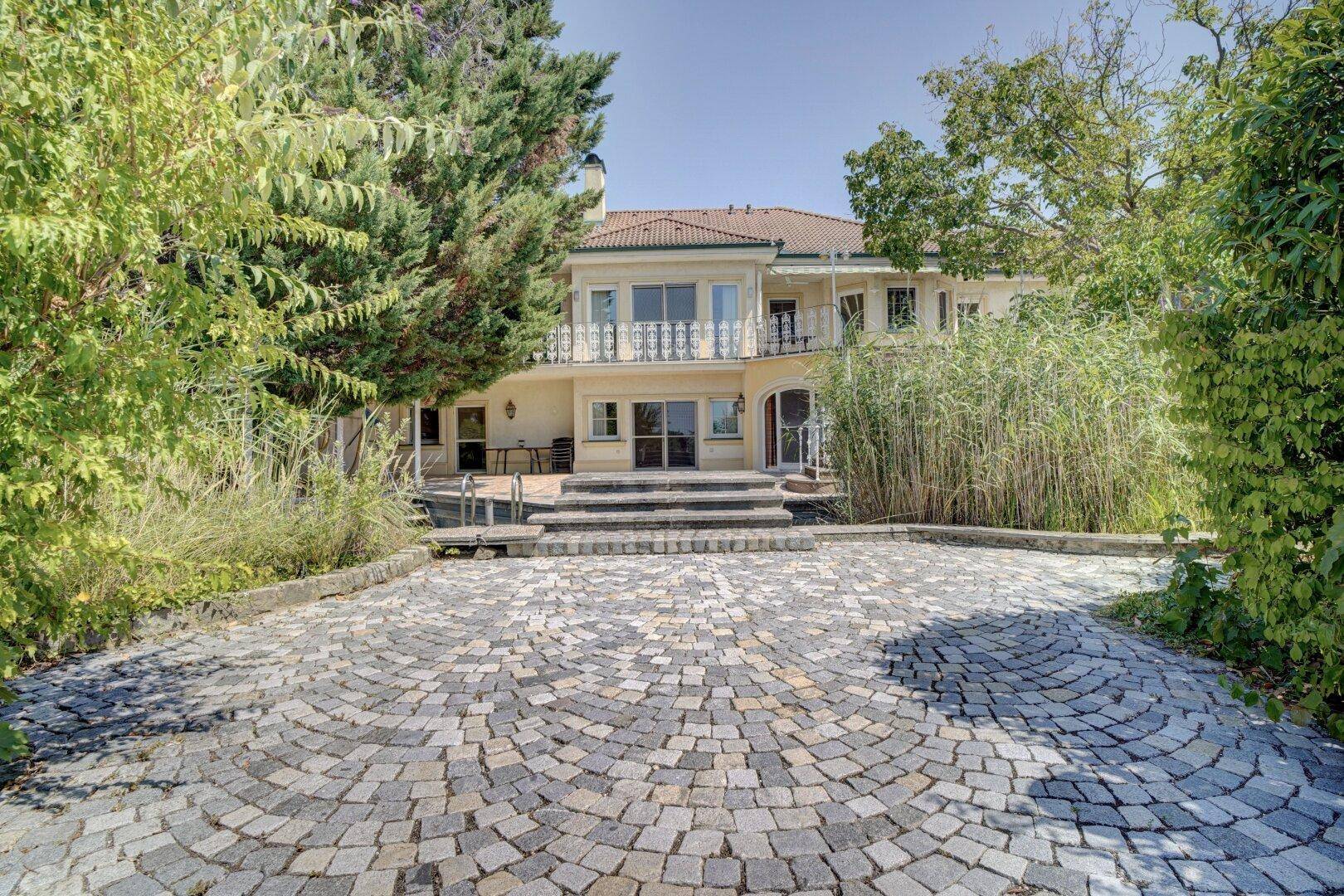 Elegante gepflasterte Auffahrt führt zum Eingang der Villa, umgeben von Grün.