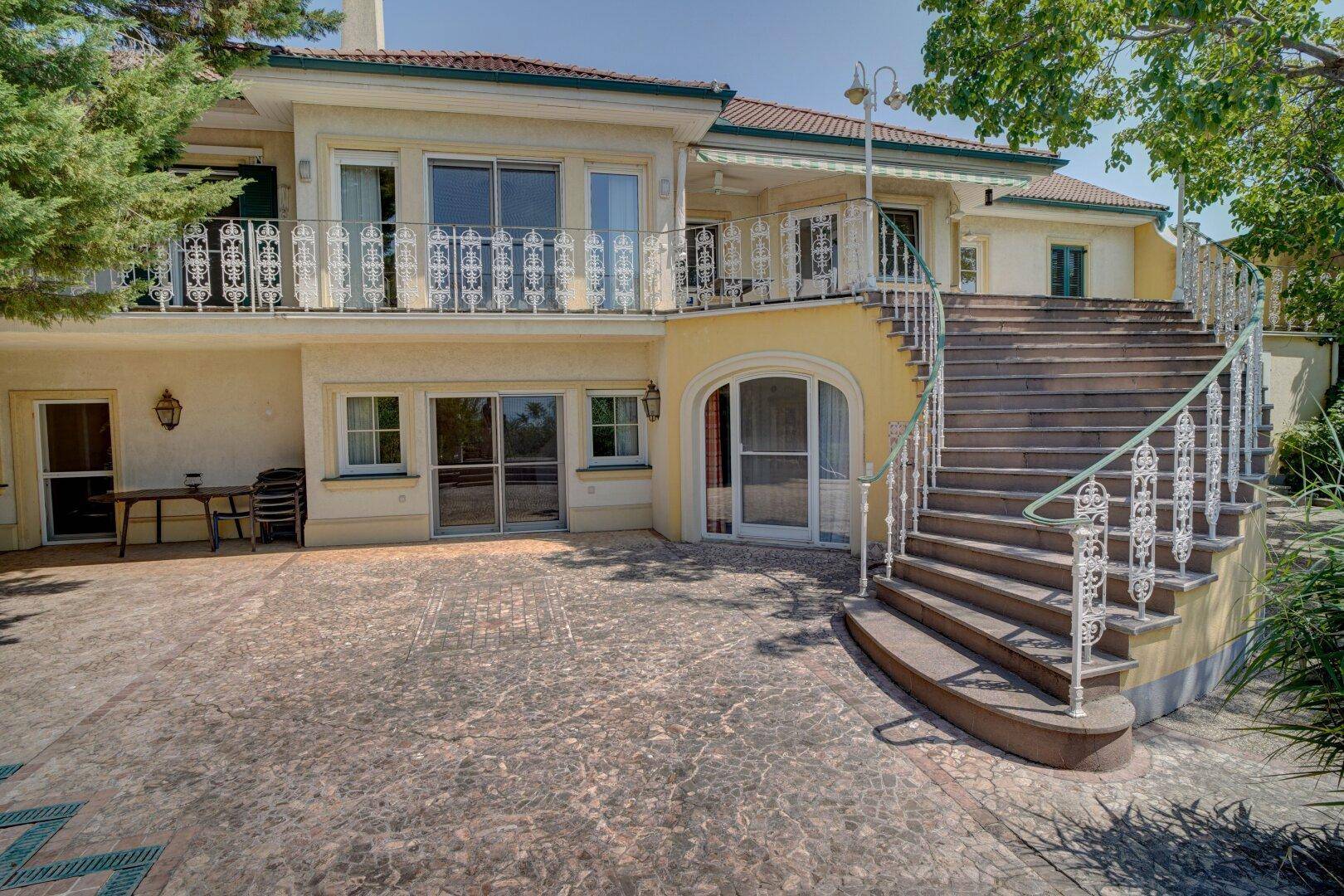 Große gepflasterte Terrasse mit imposanter Außentreppe und schmiedeeisernem Geländer.