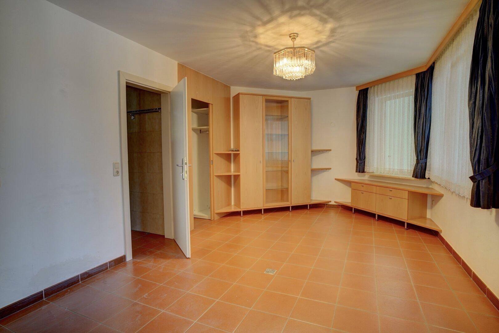 Geräumiges Schlafzimmer mit Terrakottafliesen, Einbauschrank und klassischem Kronleuchter.