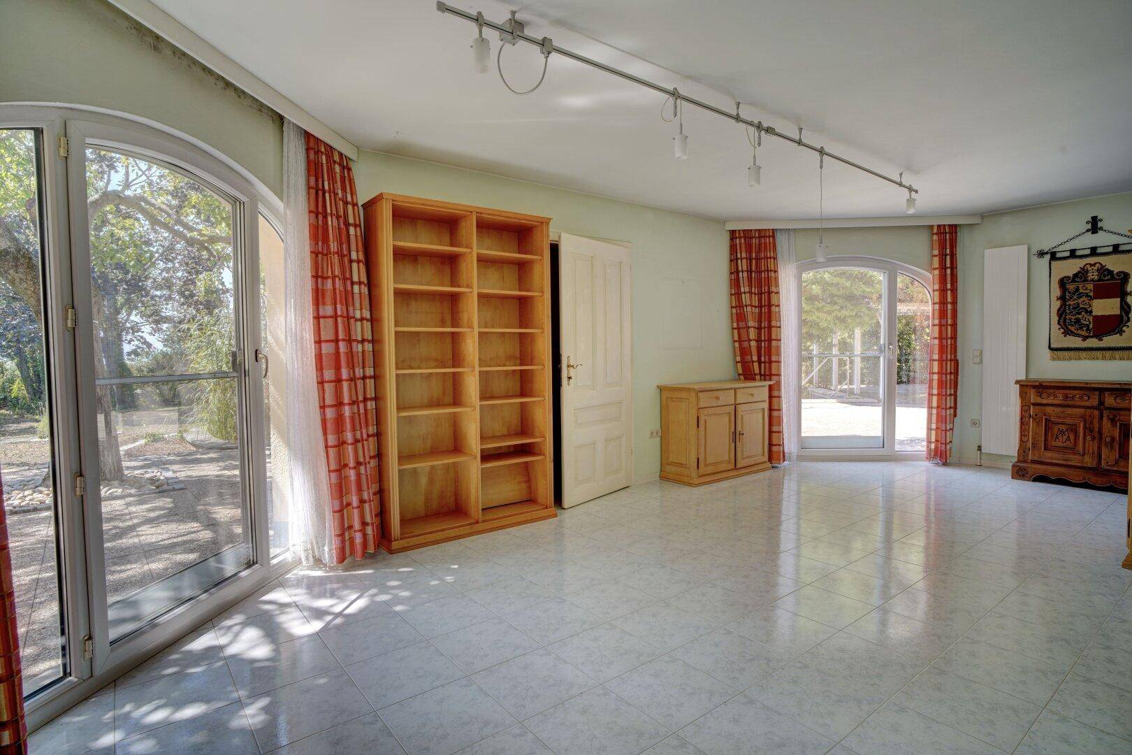 Geräumiges Wohnzimmer mit Fliesenboden, großen Fenstern und Blick ins Grüne.