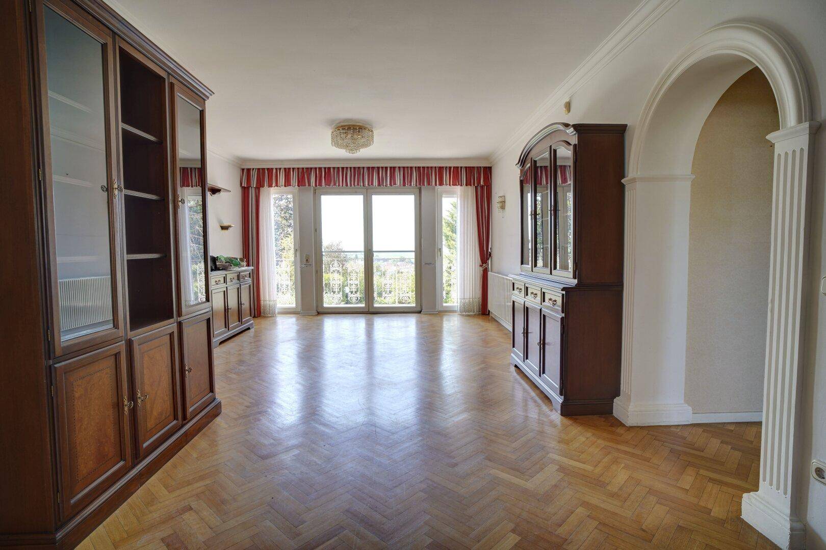 Großes Wohnzimmer mit Fischgrätparkett, klassischen Möbeln und Zugang zu einem Balkon.