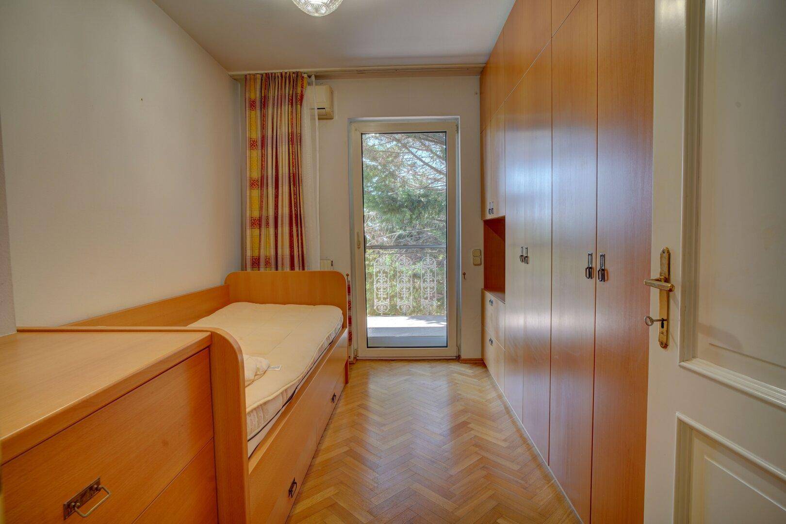 Schlafzimmer mit Einzelbett, Einbauschränken und Zugang zu einem französischen Balkon.