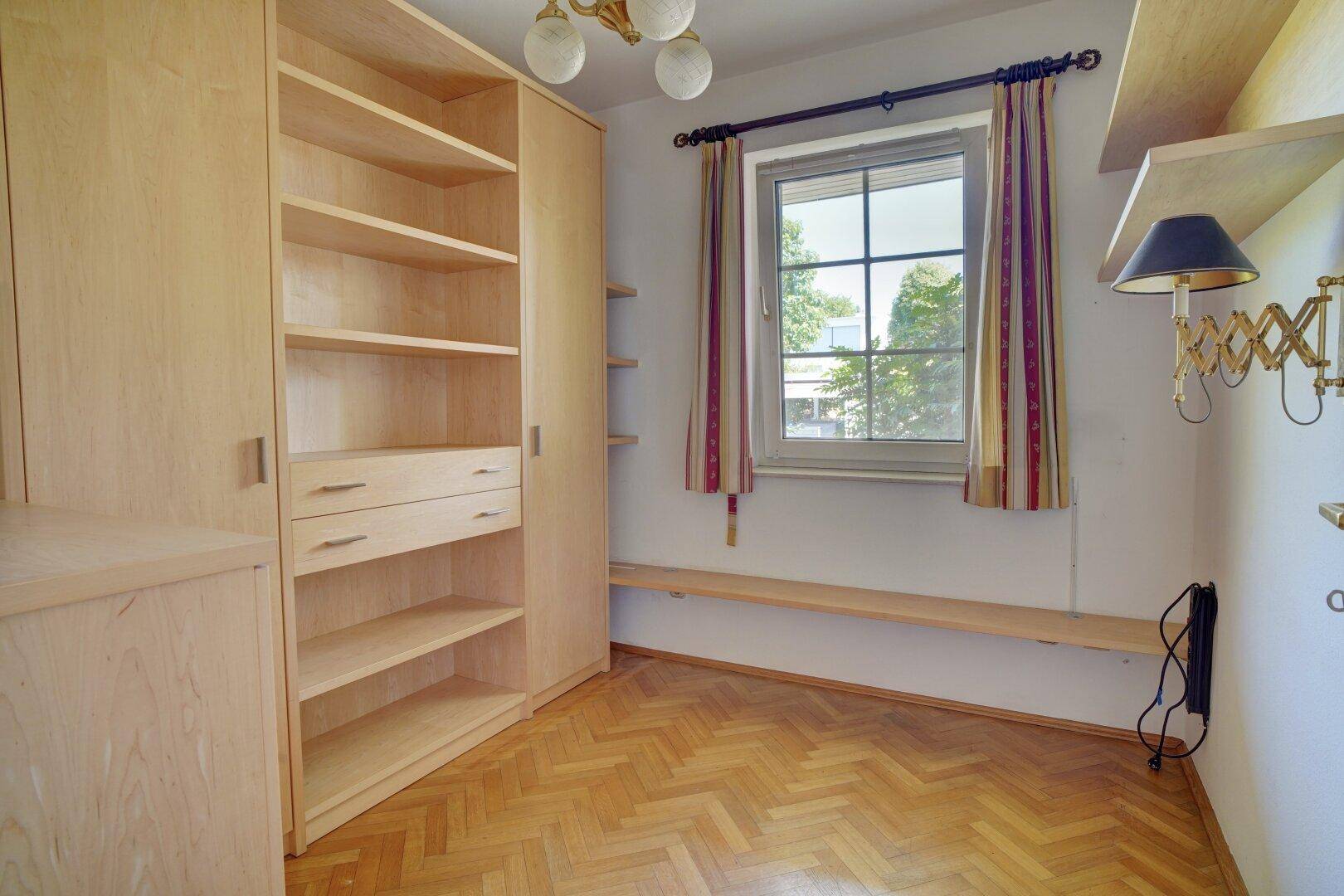 Helles Zimmer mit Parkettboden, Einbauschränken und Fensterblick ins Grüne.