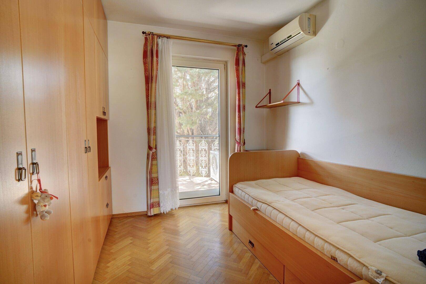 Schlafzimmer mit Parkettboden, Klimaanlage und Zugang zu einem französischen Balkon.