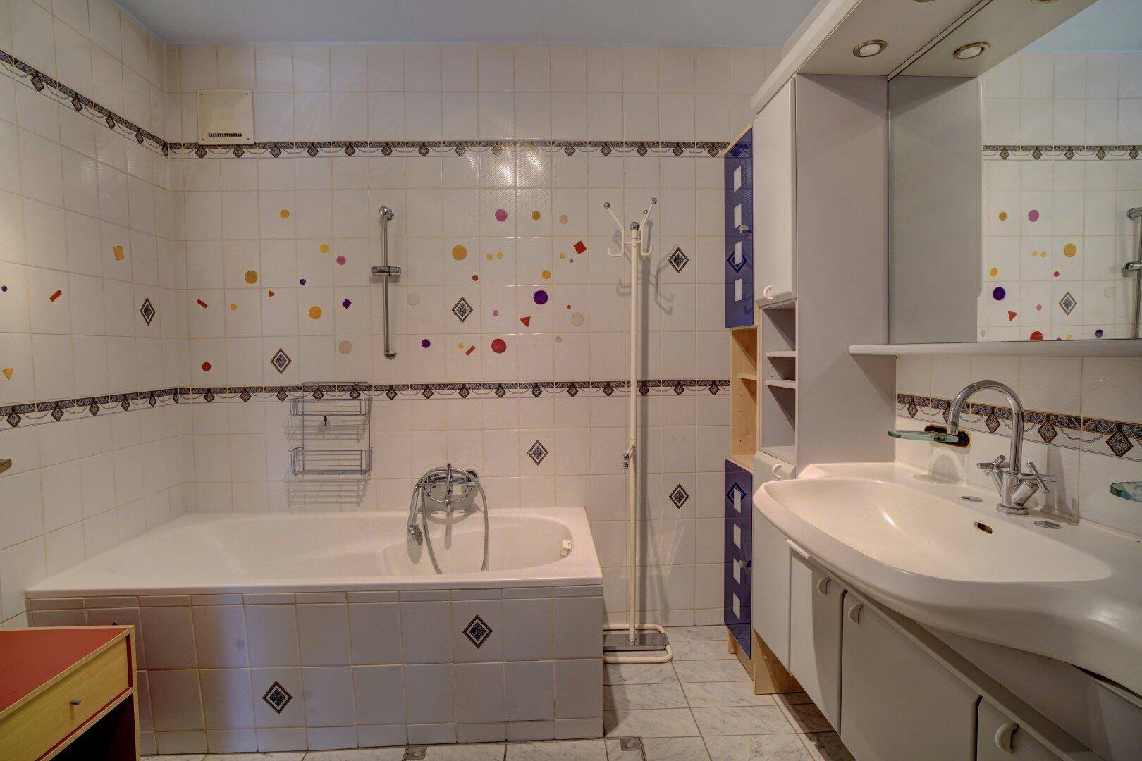 Badezimmer mit Badewanne, Waschbecken und verspielten Fliesen im 80er-Jahre-Stil.