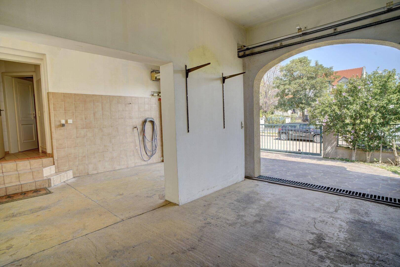 Garage mit gefliester Wand, Betonboden und Zugang zum Außenbereich des Hauses.