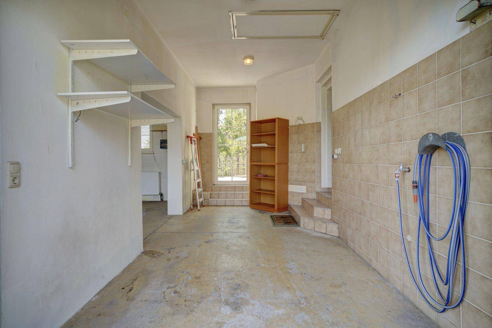 Helle Garage mit Regalen, Betonboden und Fenster zum Gartenbereich.