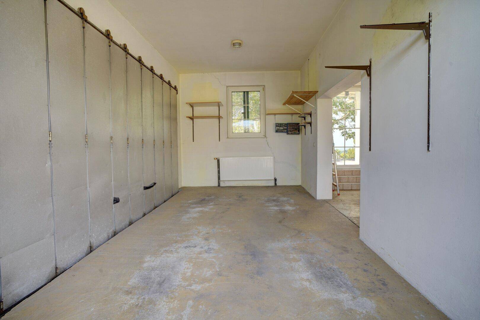 Große Garage mit Betonboden, Heizkörper und praktischen Regalen für Stauraum.