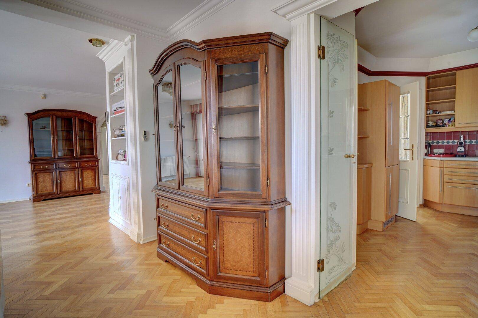 Übergangsbereich zwischen Wohnzimmer und Küche mit Holzboden und Vitrinenschrank.