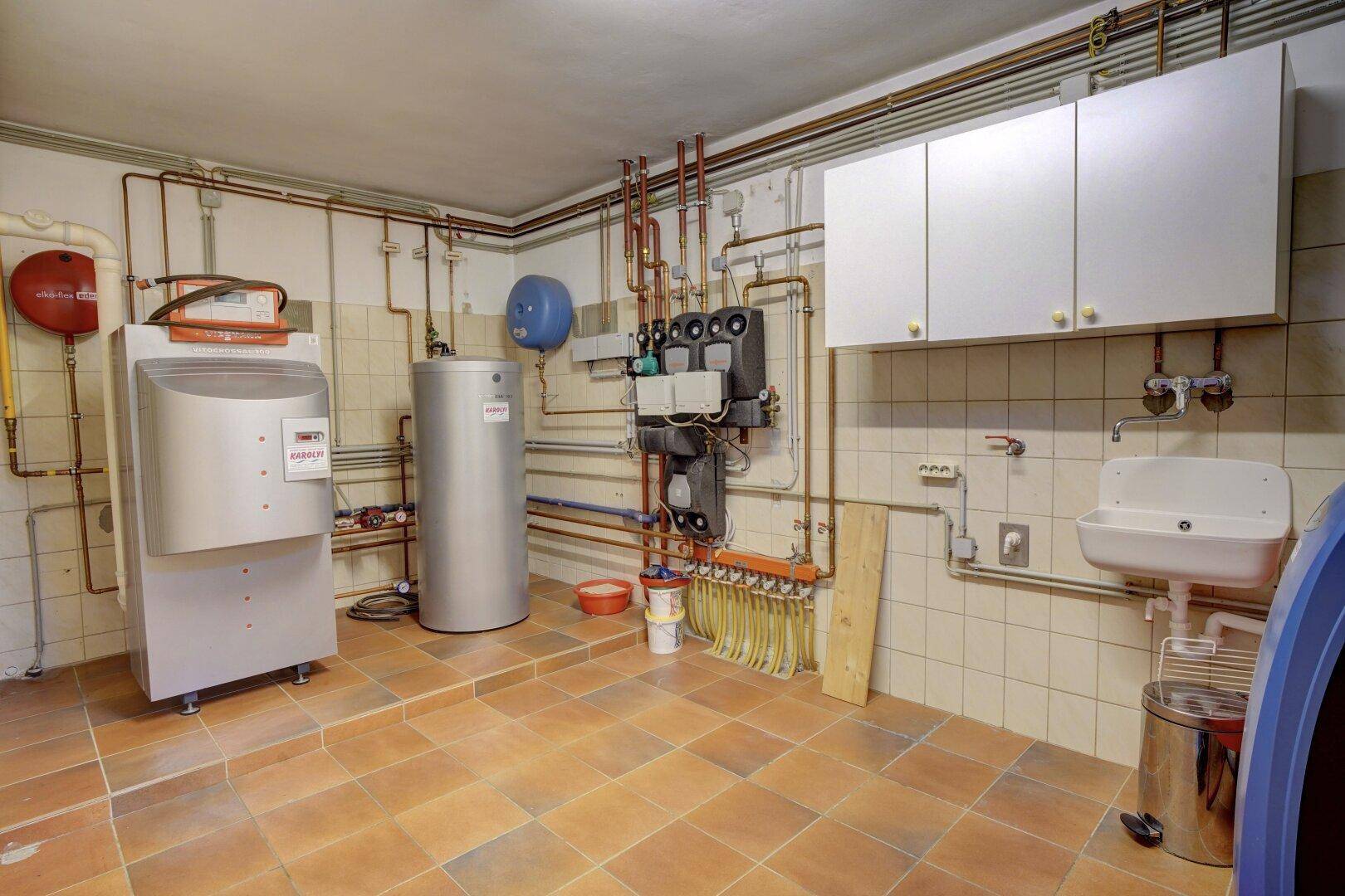 Heizungsraum mit moderner Heizungsanlage, Warmwasserspeicher und Waschbecken.