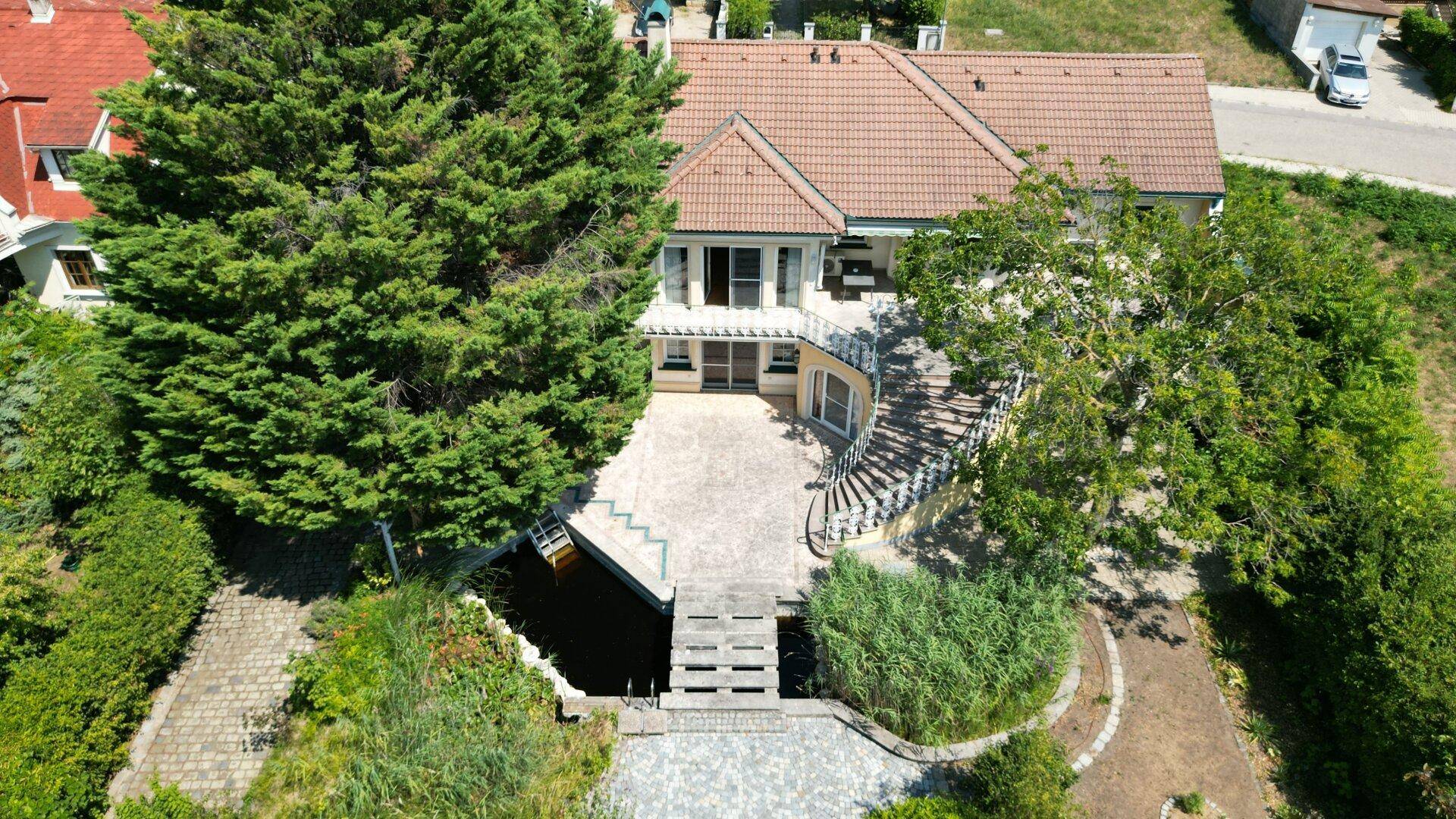 Luftaufnahme der Villa mit weitläufigem Garten, Teich und gepflasterter Auffahrt.
