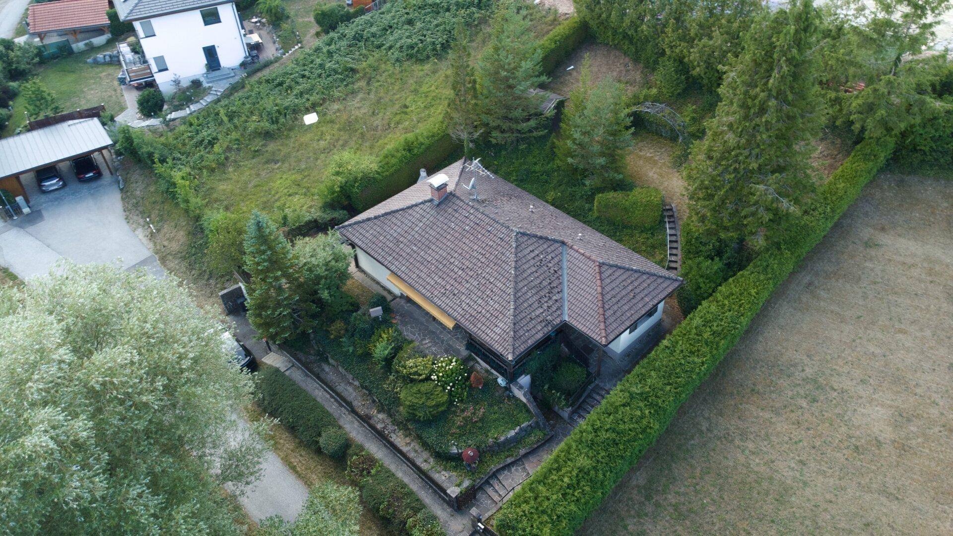 Luftaufnahme eines Einfamilienhauses mit großem, grünen Grundstück und umliegender Natur.