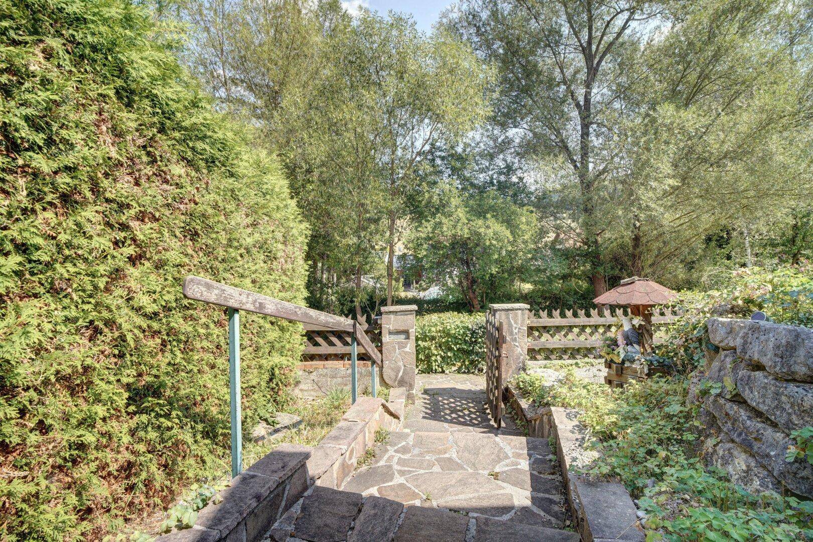 Steintreppe und Pfad führen durch den gepflegten Garten mit Hecken und Bäumen.