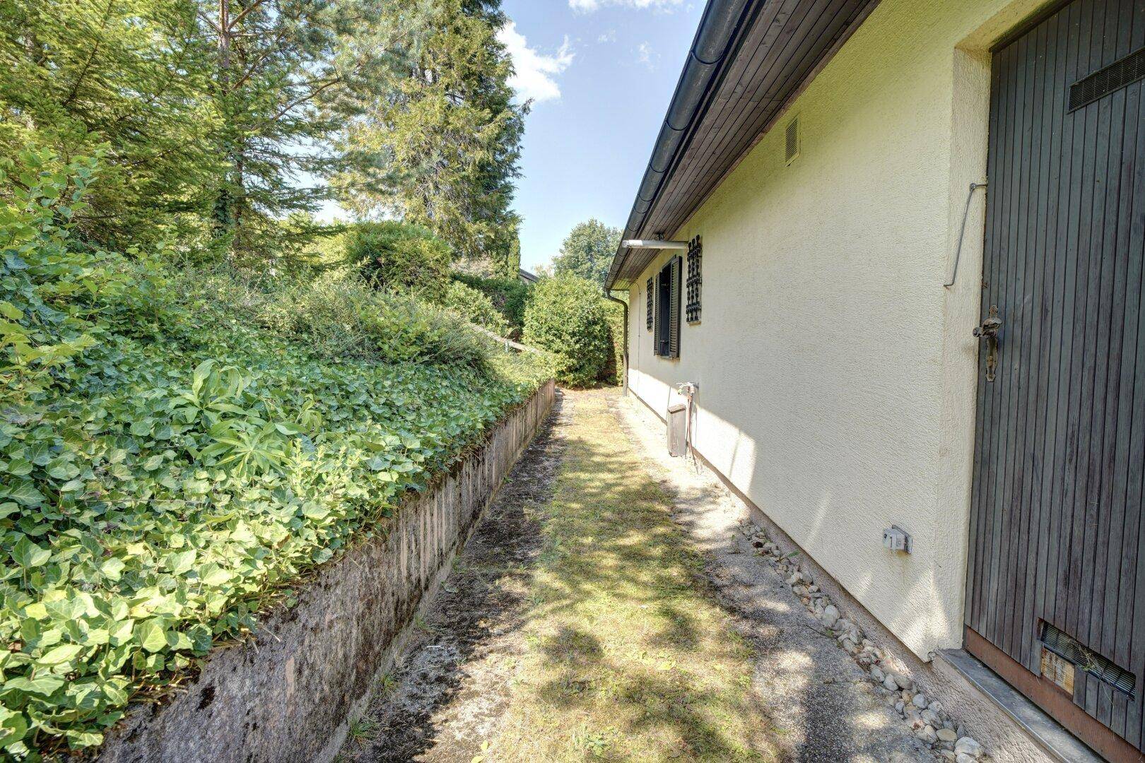 Seitenansicht des Hauses mit schmalem Gartenweg und Holztür.