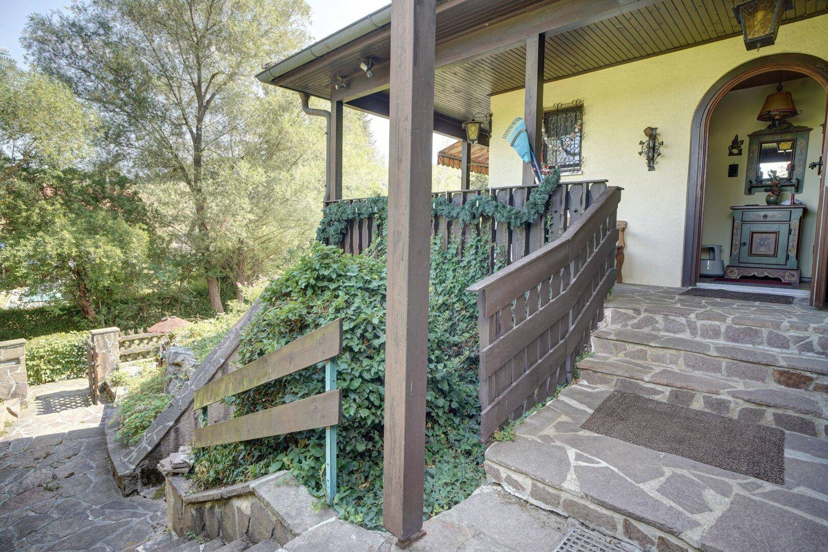 Steintreppe führt zum überdachten Eingangsbereich des Hauses, umgeben von Grün.