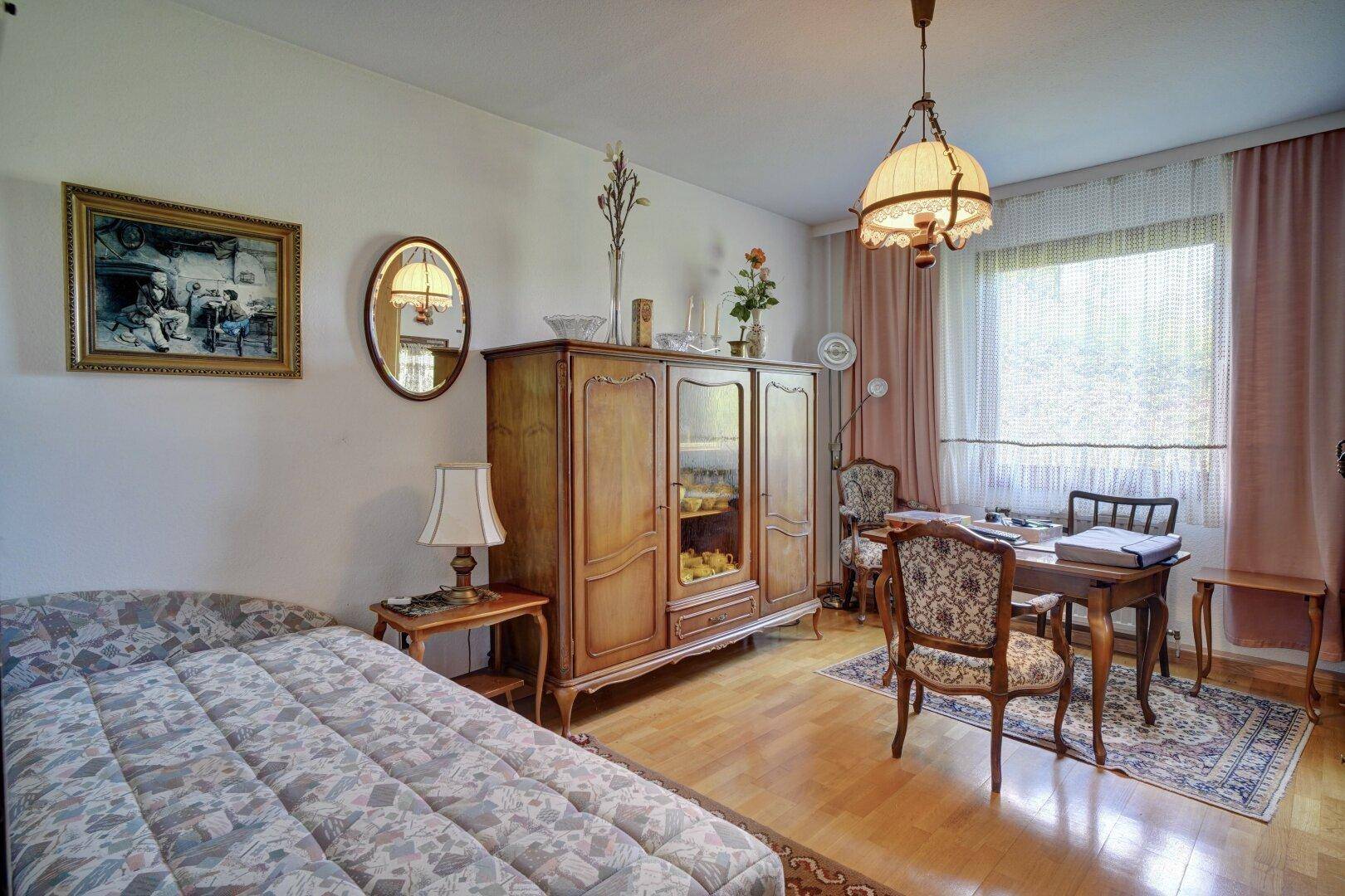 Schlafzimmer mit Holzboden, großem Kleiderschrank und Schreibtisch am Fenster.