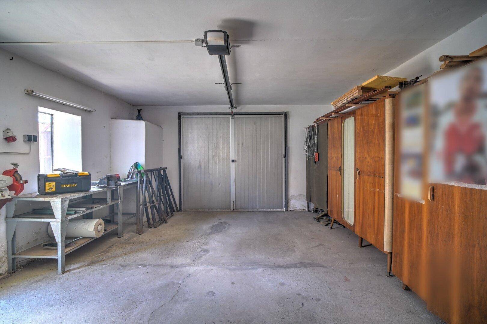 Geräumige Garage mit Werkbank, Werkzeugen und einem großen Garagentor, ideal für Hobby und Lagerung.