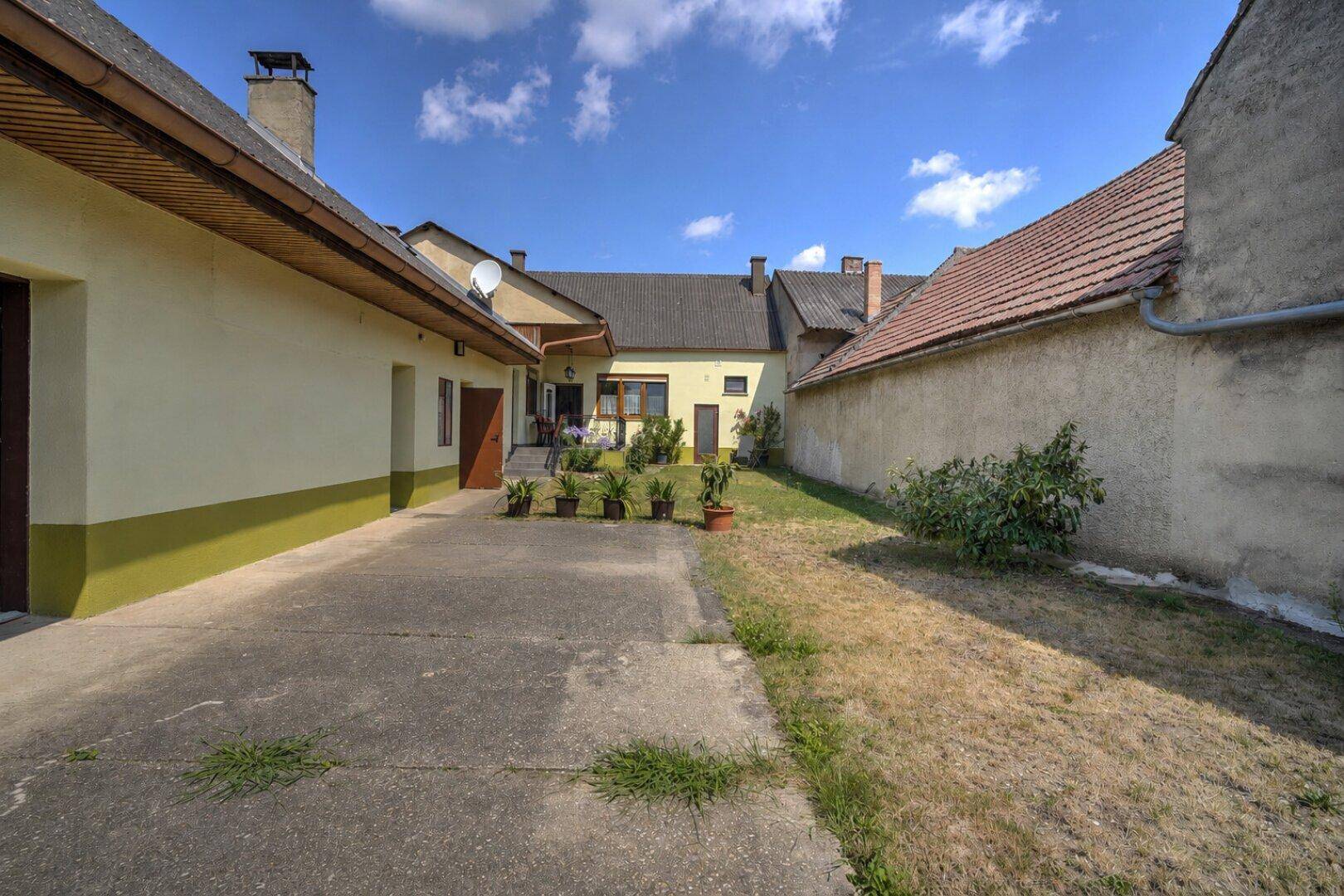Ansicht des ländlichen Gebäudes mit gepflastertem Bereich und trockenem Rasen unter blauem Himmel.