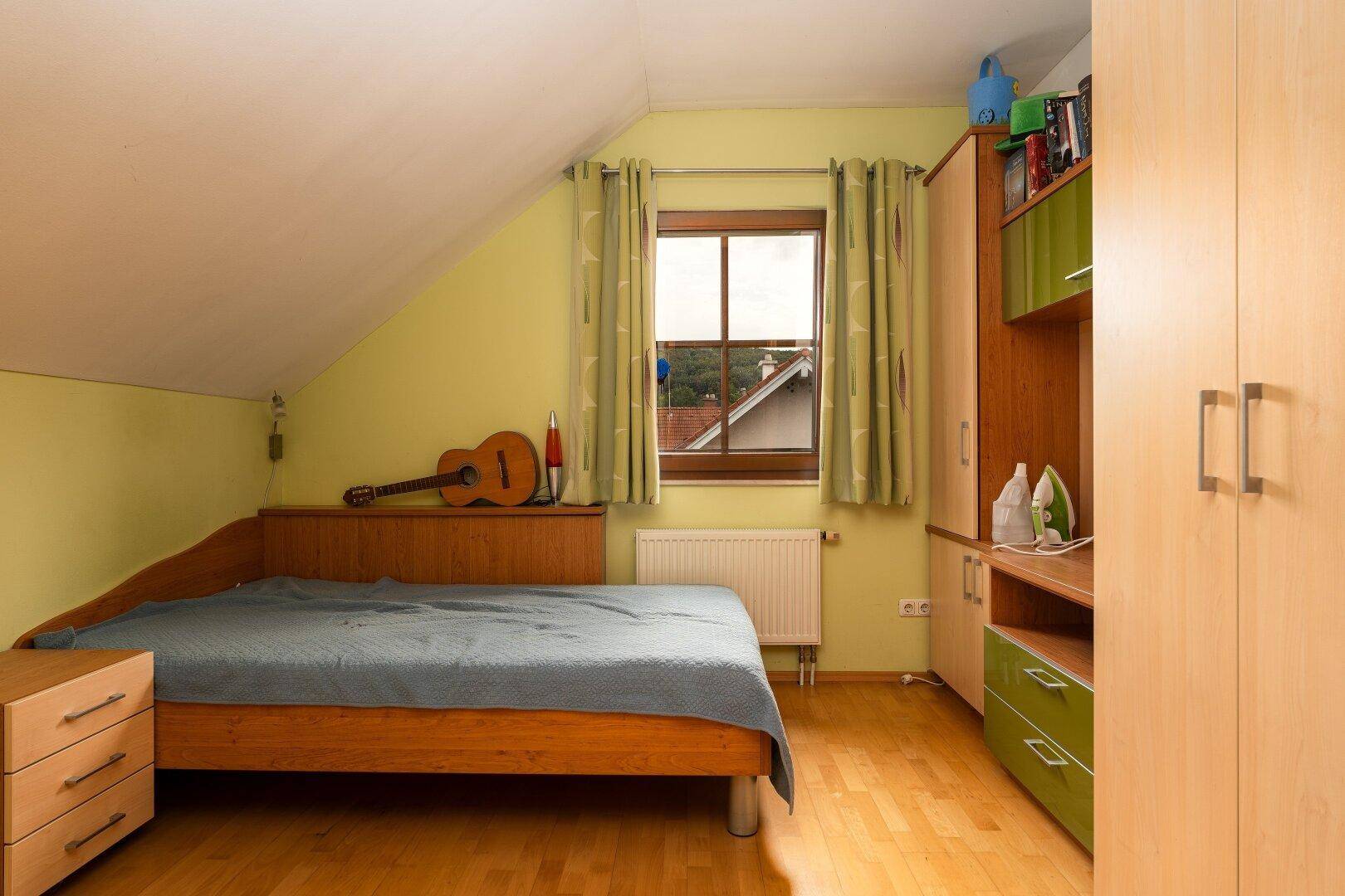 Helles Schlafzimmer im Dachgeschoss mit Holzbett, Schrank und Fenster mit Blick ins Grüne.