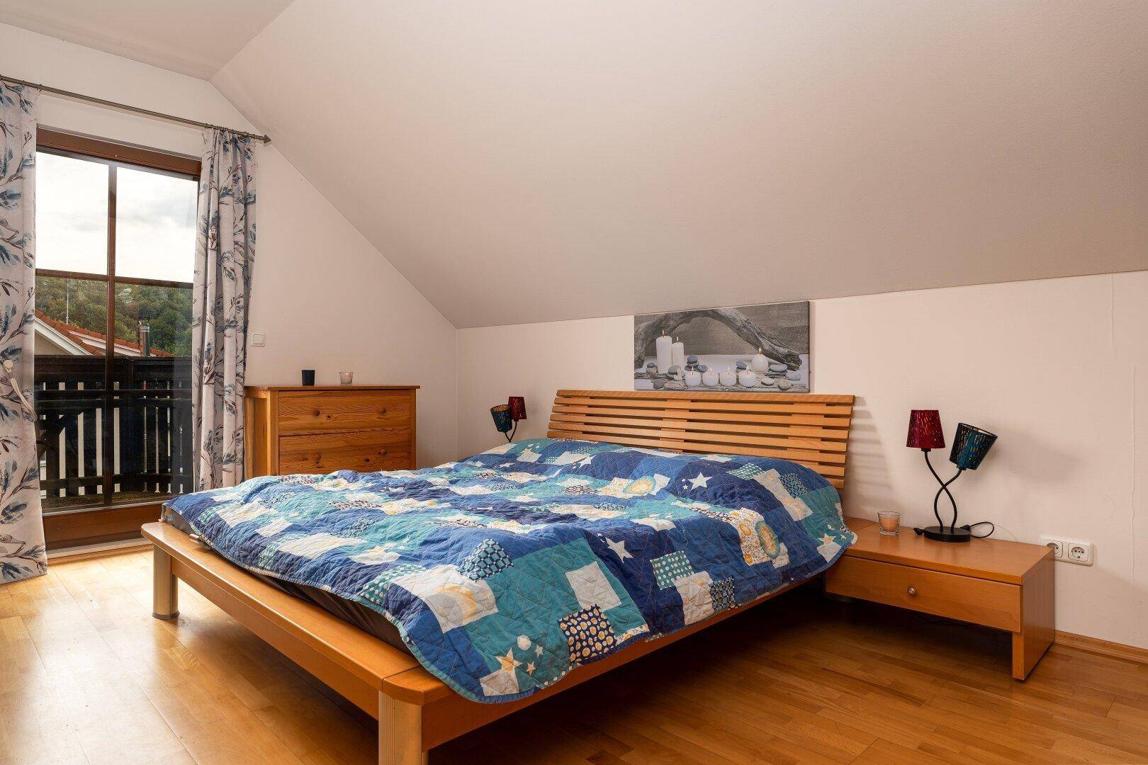 Gemütliches Schlafzimmer im Dachgeschoss mit Holzbett, Nachttischen und Zugang zu einem französischen Balkon.