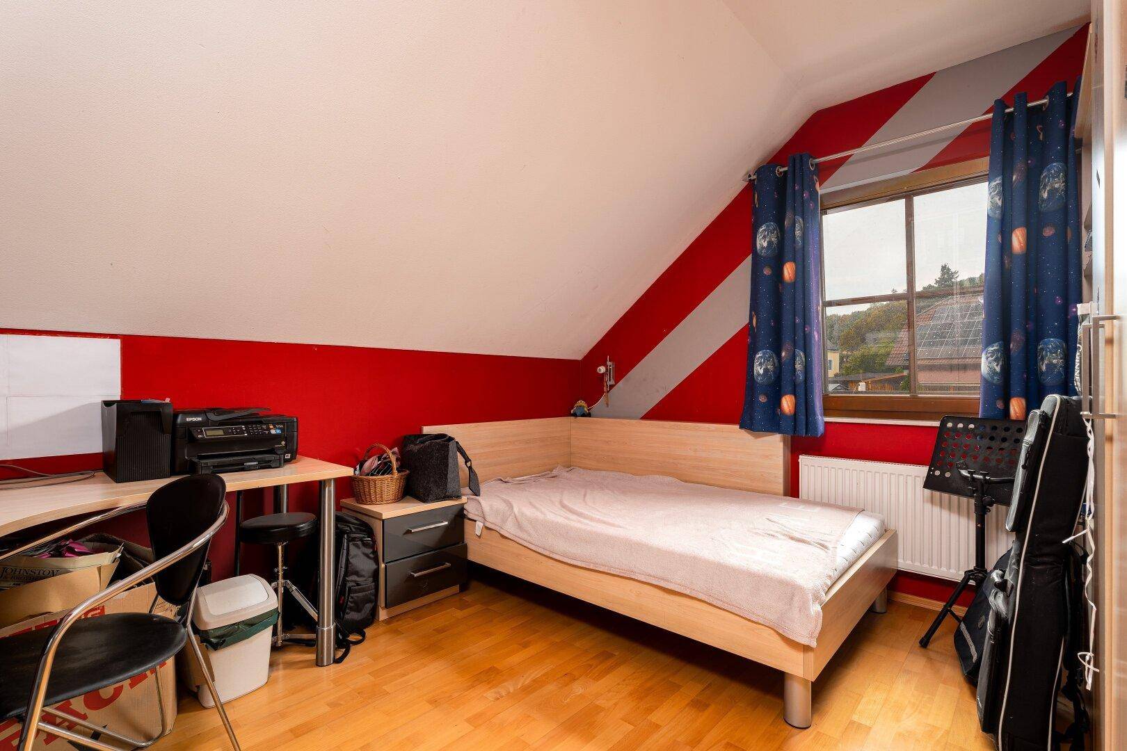 Jugendzimmer im Dachgeschoss mit Einzelbett, Schreibtisch und farbenfroher Wandgestaltung.