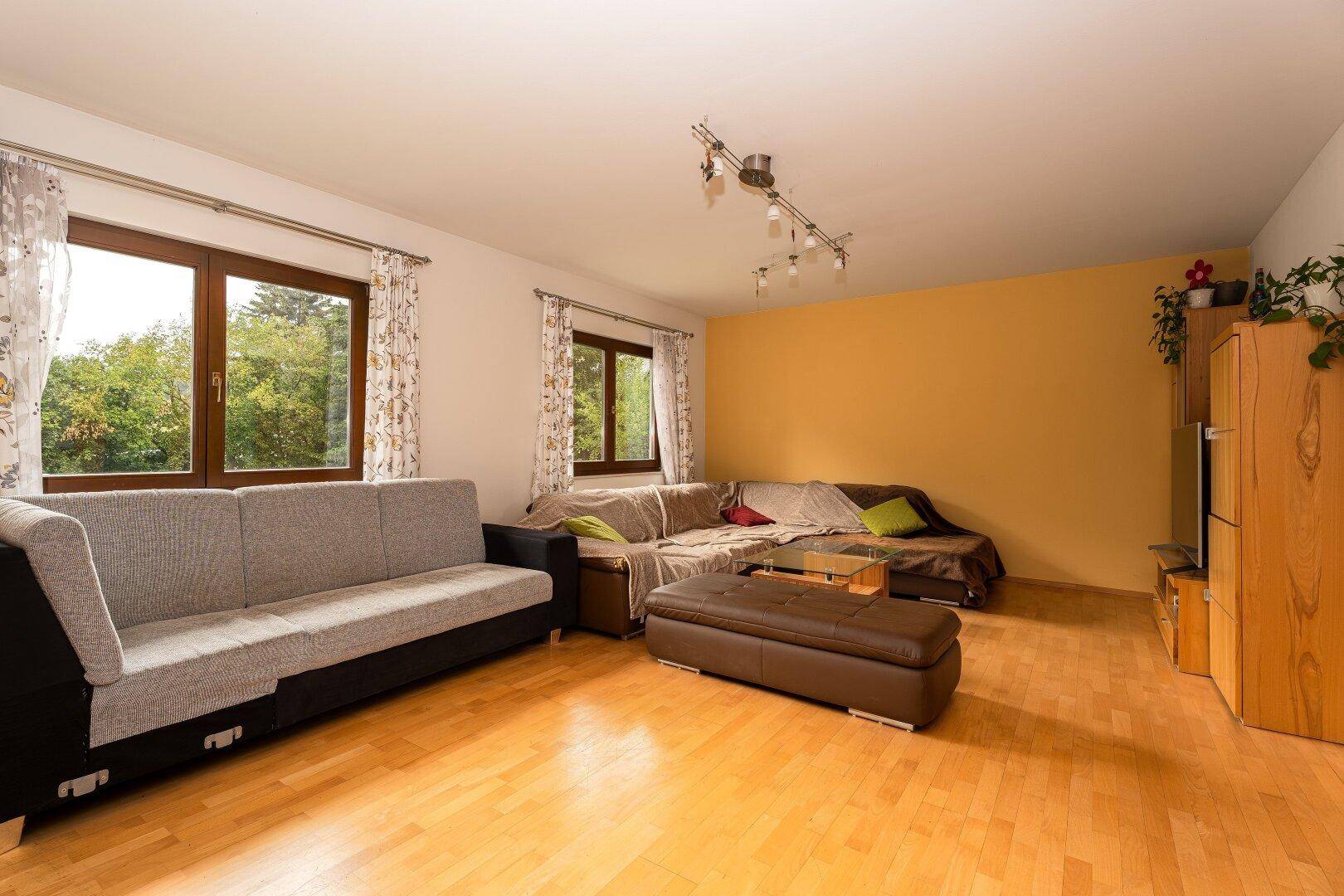Geräumiges Wohnzimmer mit Holzboden, bequemen Sofas und Blick ins Grüne durch große Fenster.
