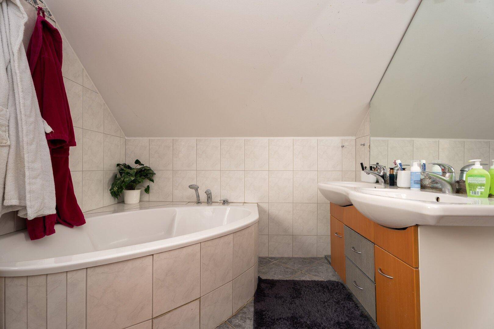 Badezimmer im Dachgeschoss mit Eckbadewanne, Doppelwaschbecken und großem Spiegel.