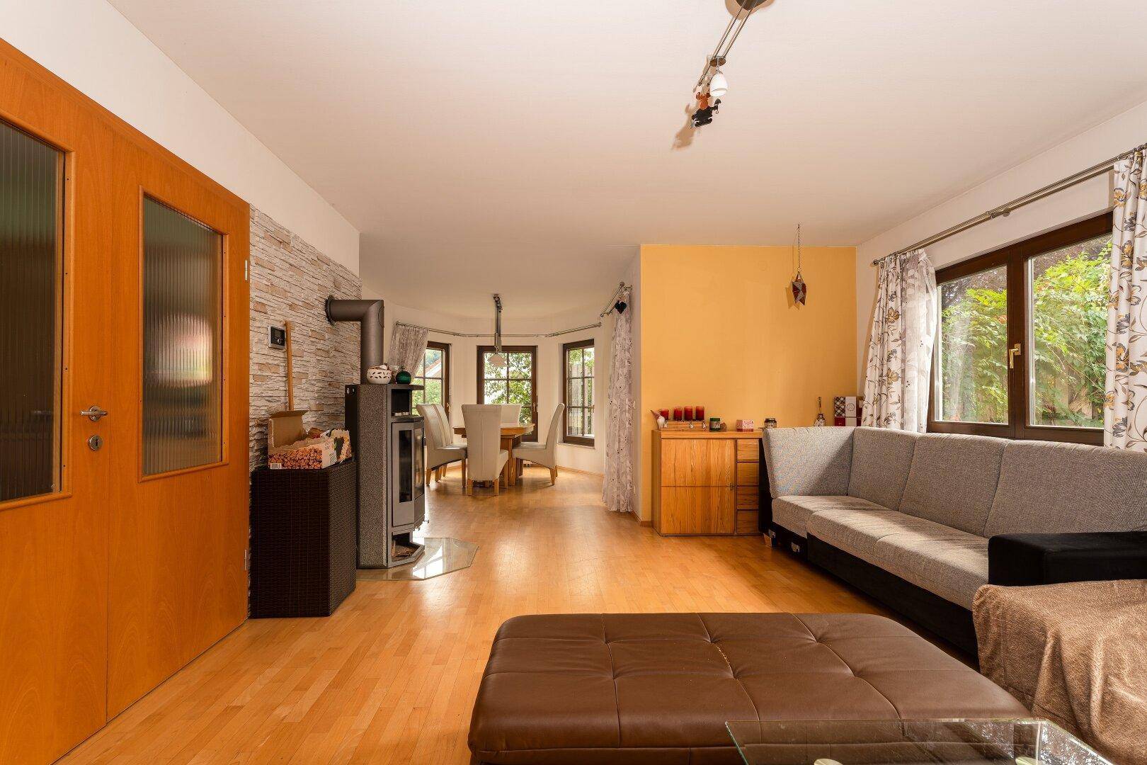 Wohnzimmer mit Holzboden, modernem Holzofen und offenem Übergang zum Essbereich.