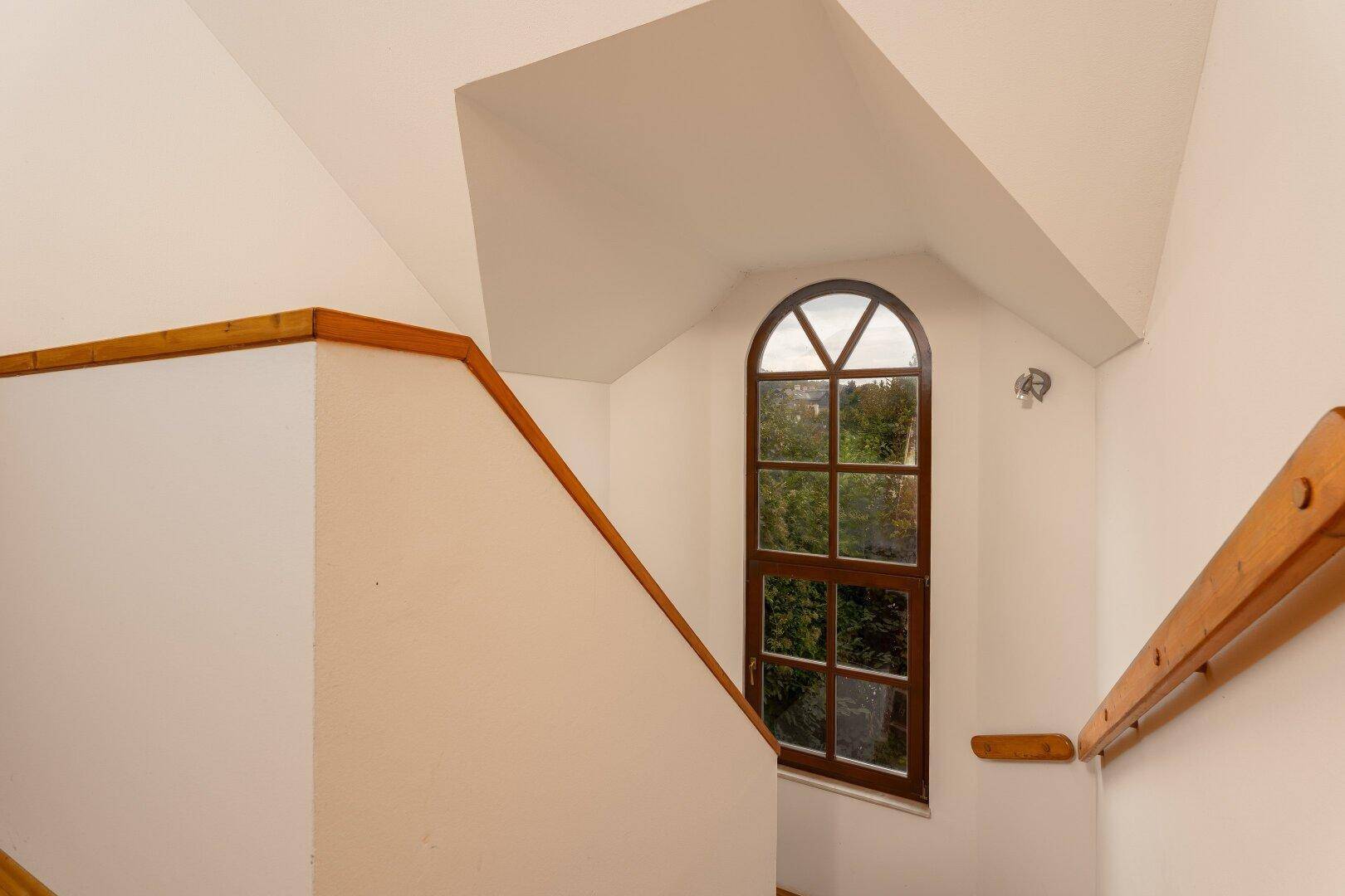 Helles Treppenhaus mit einem großen, bogenförmigen Fenster, das viel Tageslicht spendet.