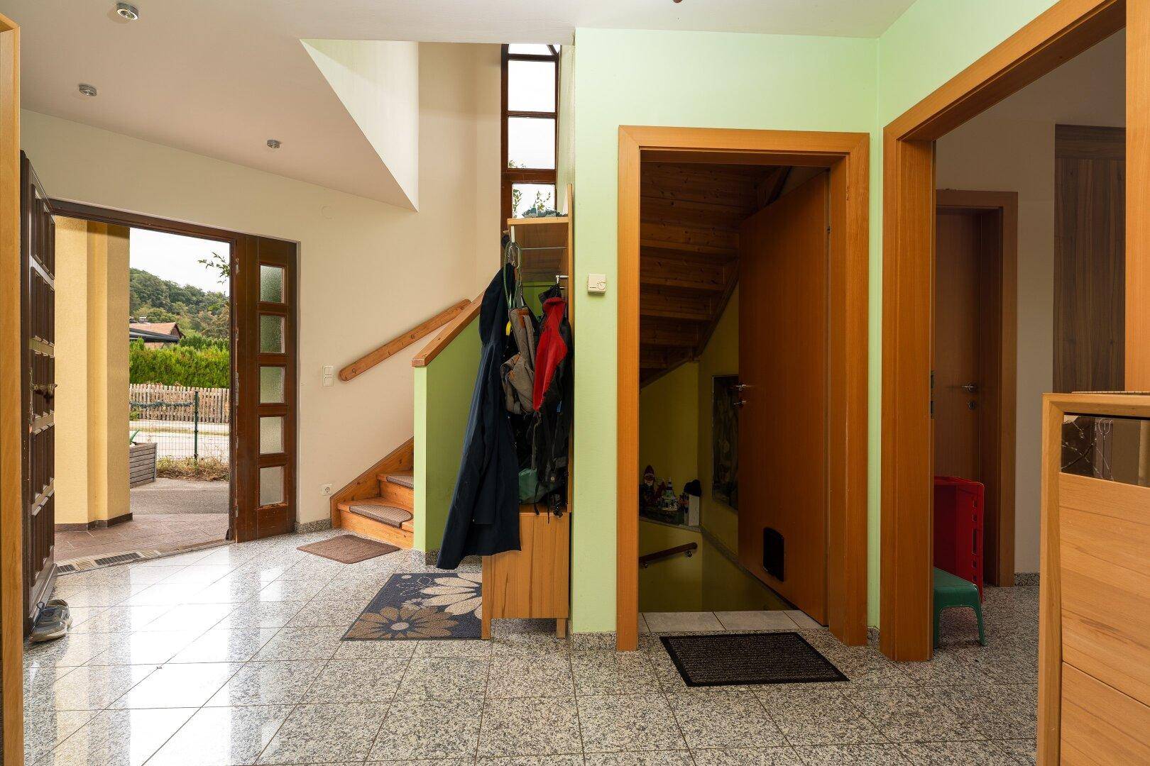 Heller Eingangsbereich mit Fliesenboden, Garderobe und Holztreppe zum Obergeschoss.
