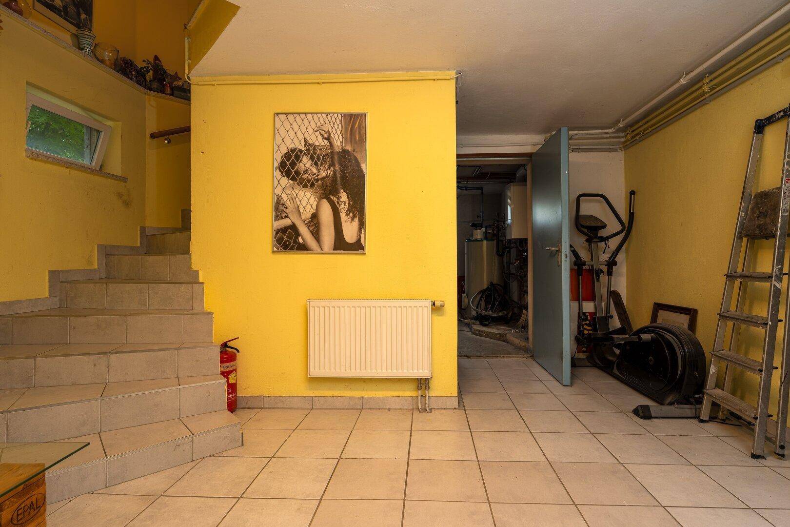 Ausgebauter Kellerbereich mit Fliesenboden, Treppe und Zugang zu einem Fitnessbereich.