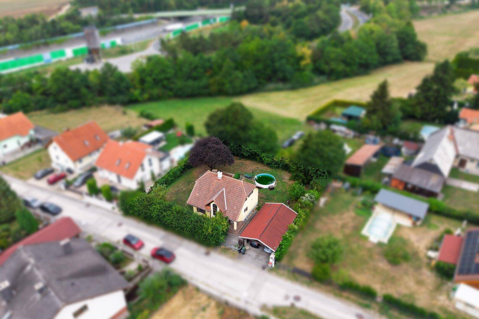 Vogelperspektive eines Hauses mit Garten, Pool und Carport, umgeben von weiteren Häusern und Natur.