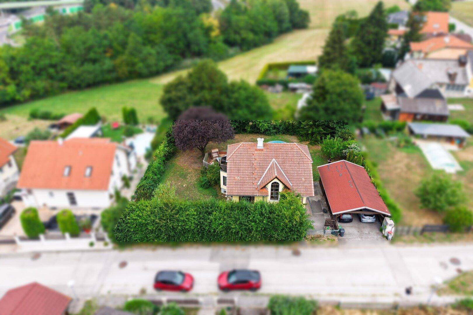 Luftaufnahme eines Einfamilienhauses mit Garten, Carport und der umliegenden Wohngegend.