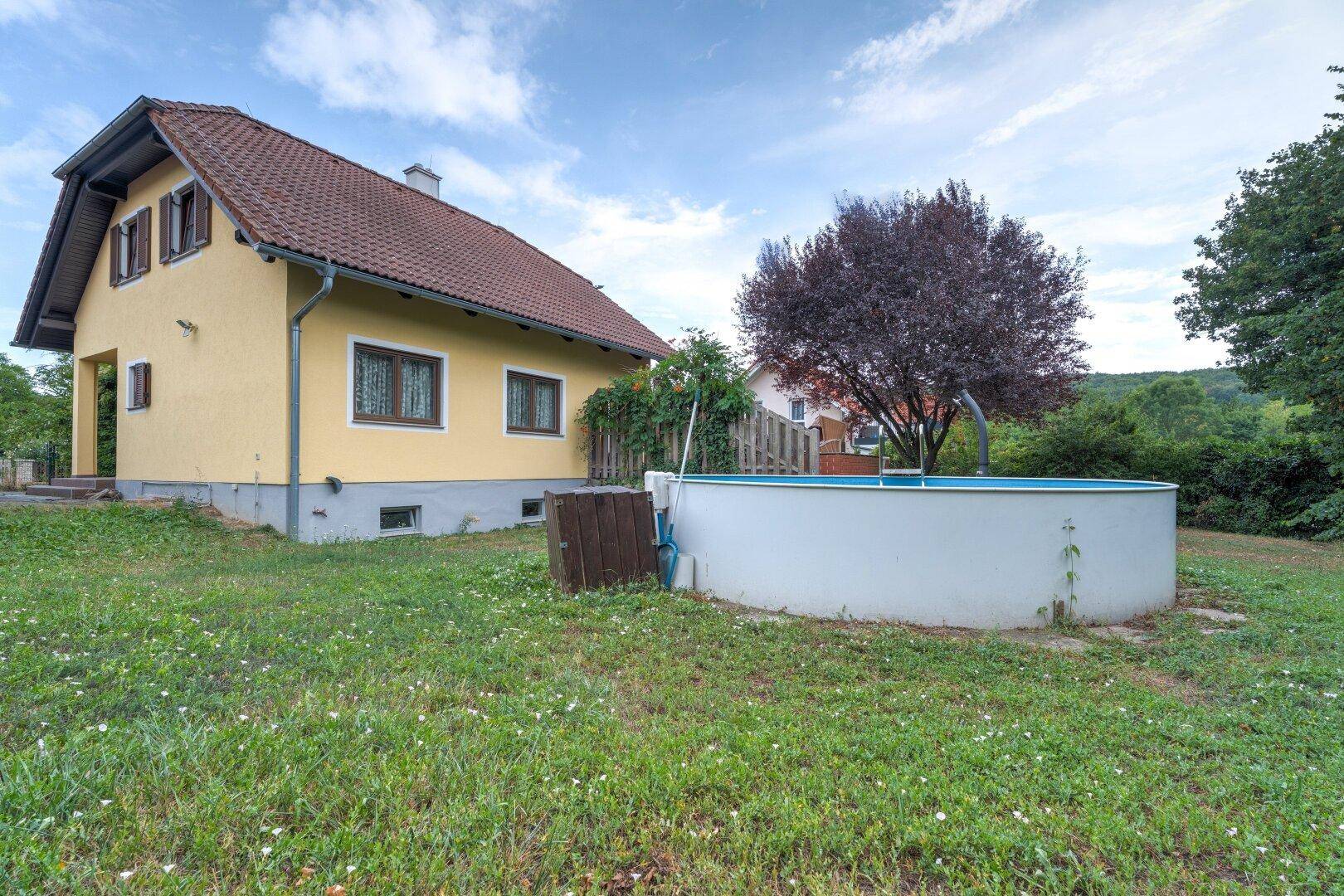 Hausansicht vom Garten mit großem Rasenbereich und einem runden Aufstellpool.
