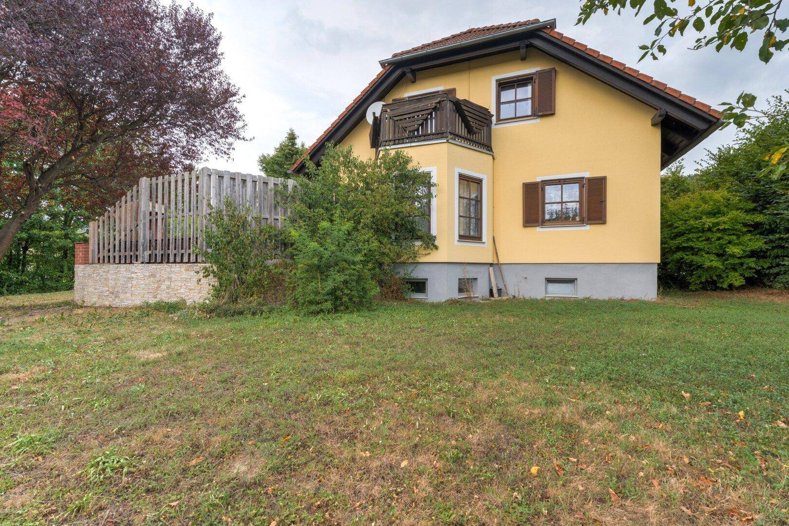 Seitenansicht des gelben Hauses mit braunen Fensterläden und einem kleinen Balkon.