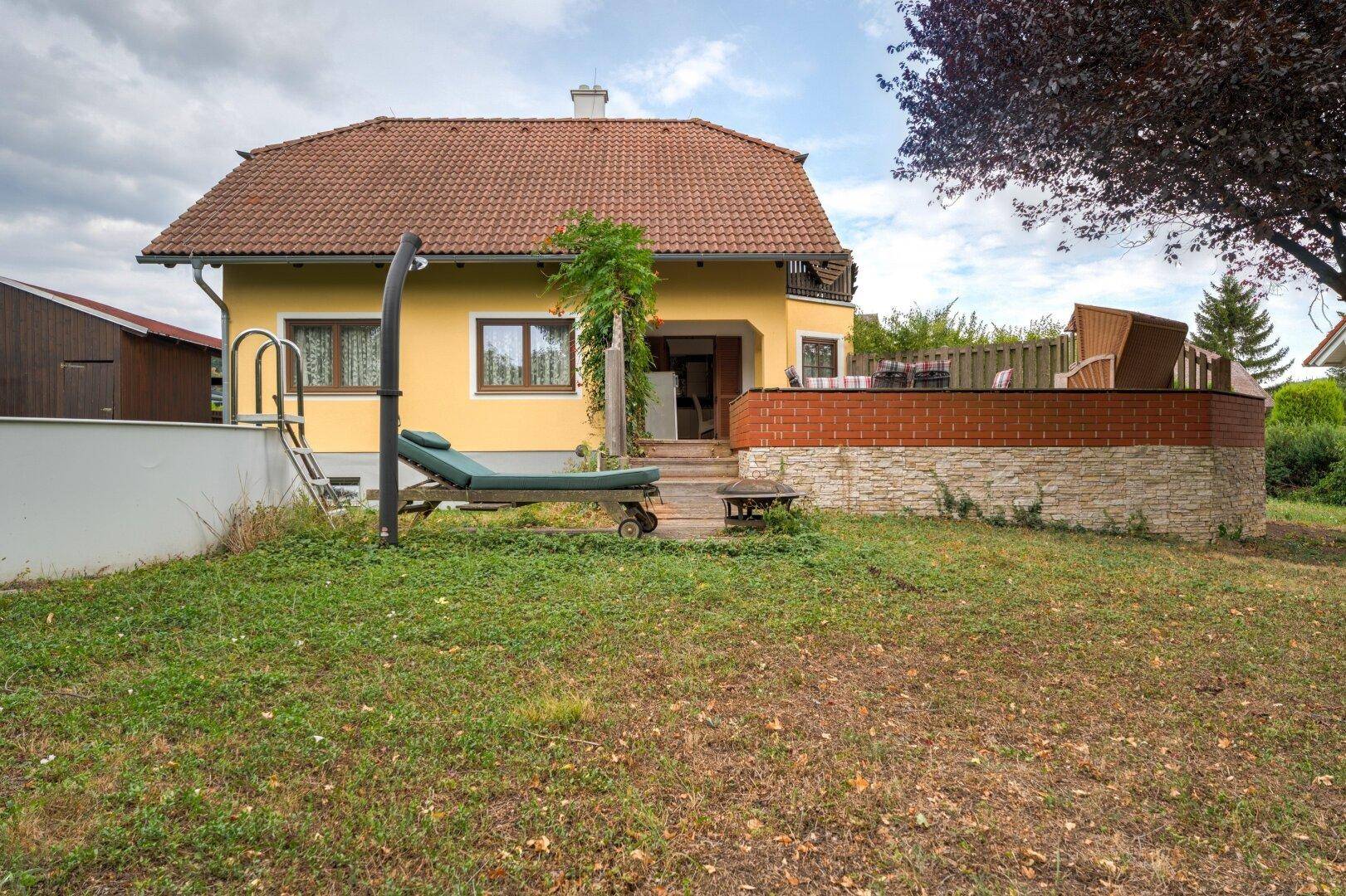 Hinterer Gartenbereich mit Pool, Sonnenliege und einer möblierten Terrasse am Haus.