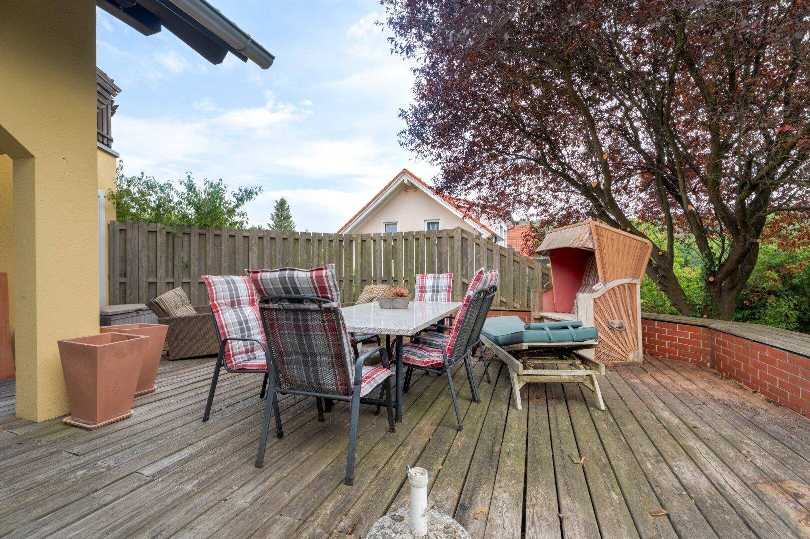 Holzterrasse mit Esstisch, Strandkorb und Blick auf den Garten.