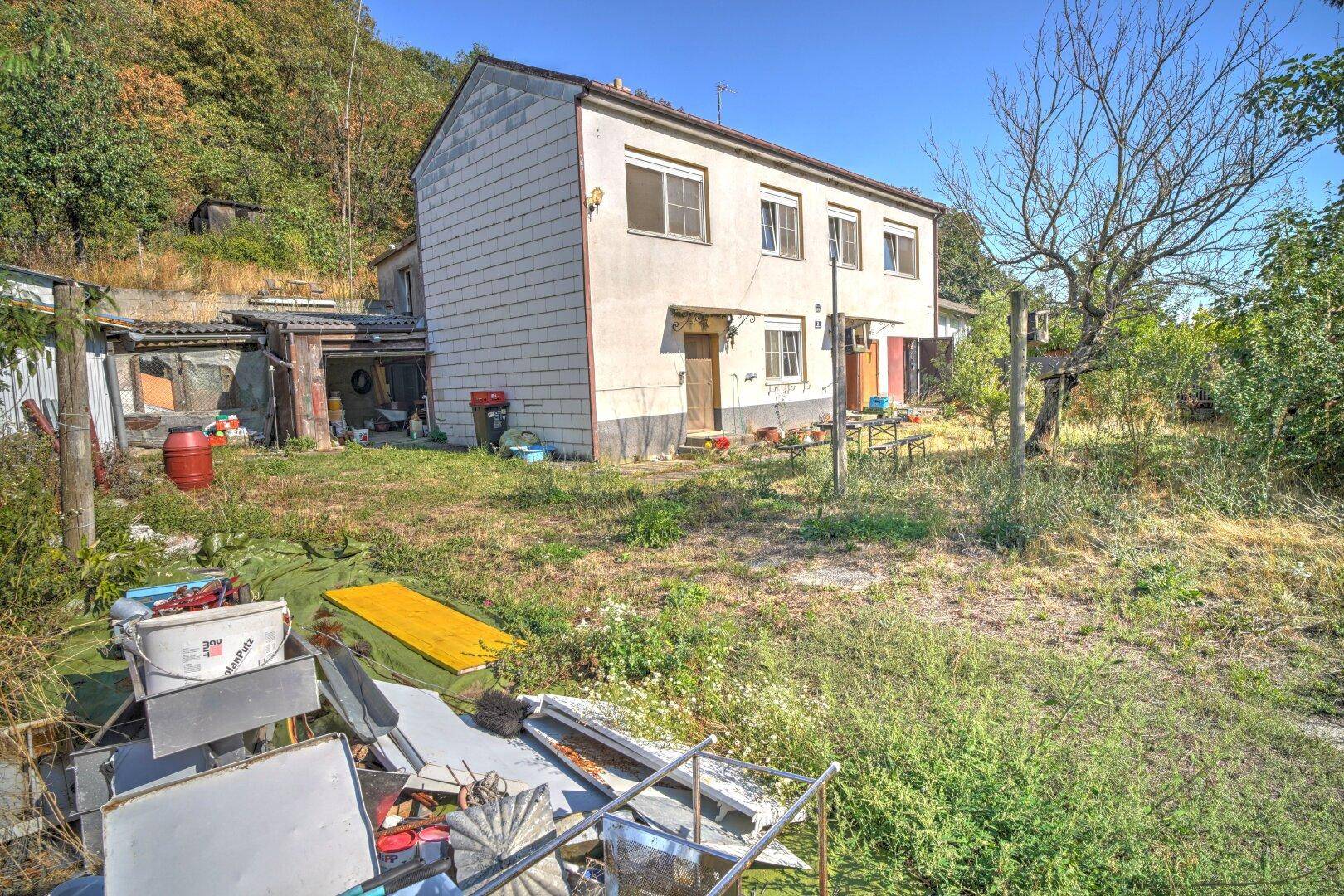 Blick auf das Haus und den Gartenbereich mit verschiedenen Gegenständen im Vordergrund und viel Grün.