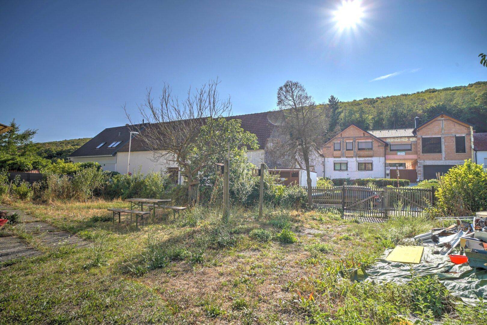 Weitläufiger Blick vom Garten auf die Nachbarhäuser und die grüne, hügelige Landschaft unter strahlender Sonne.