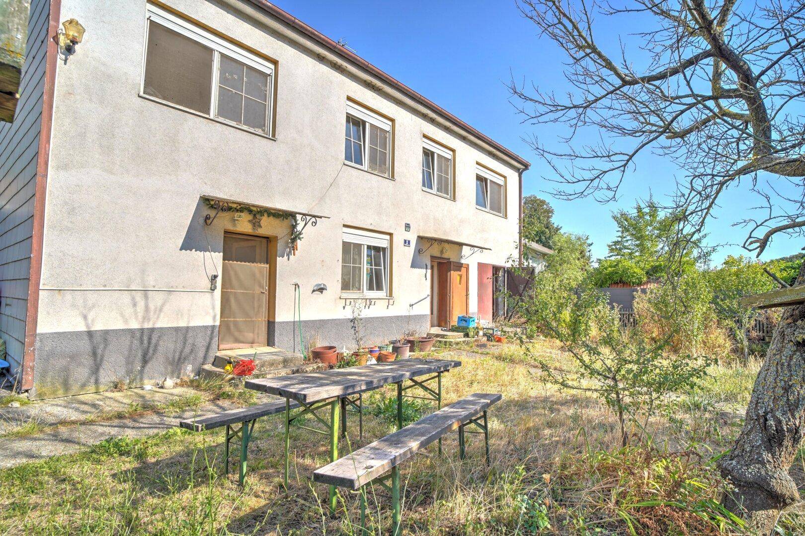 Vorderansicht des Hauses mit einem einfachen Picknicktisch im naturbelassenen Gartenbereich.
