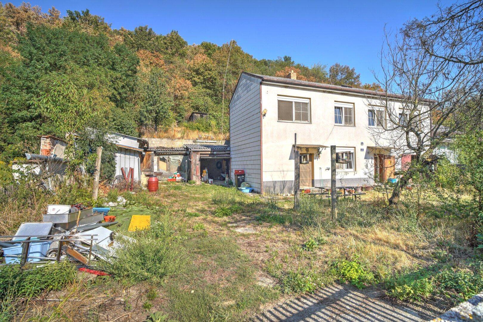 Rückansicht des Hauses mit dem weitläufigen Garten, Nebengebäuden und dem bewaldeten Hang.