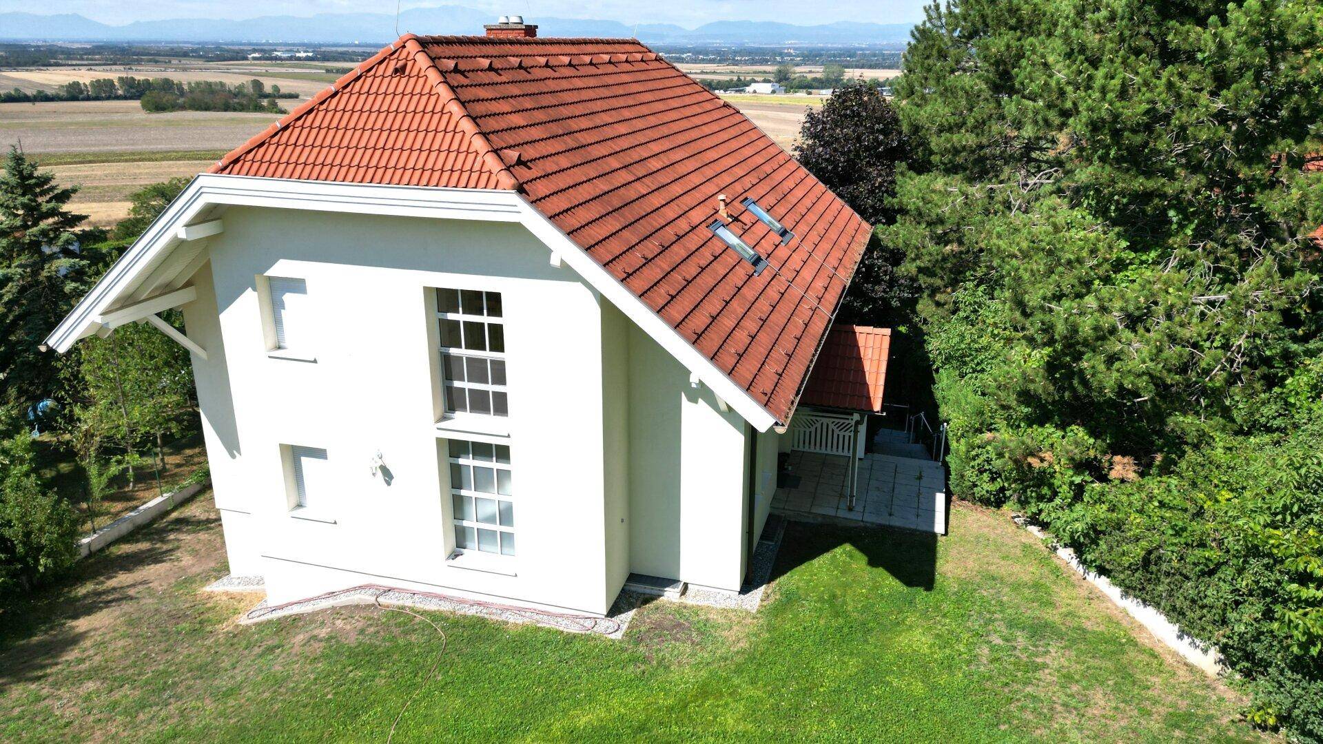 Seitenansicht des Einfamilienhauses mit rotem Ziegeldach und großen Fenstern, umgeben von Grün.