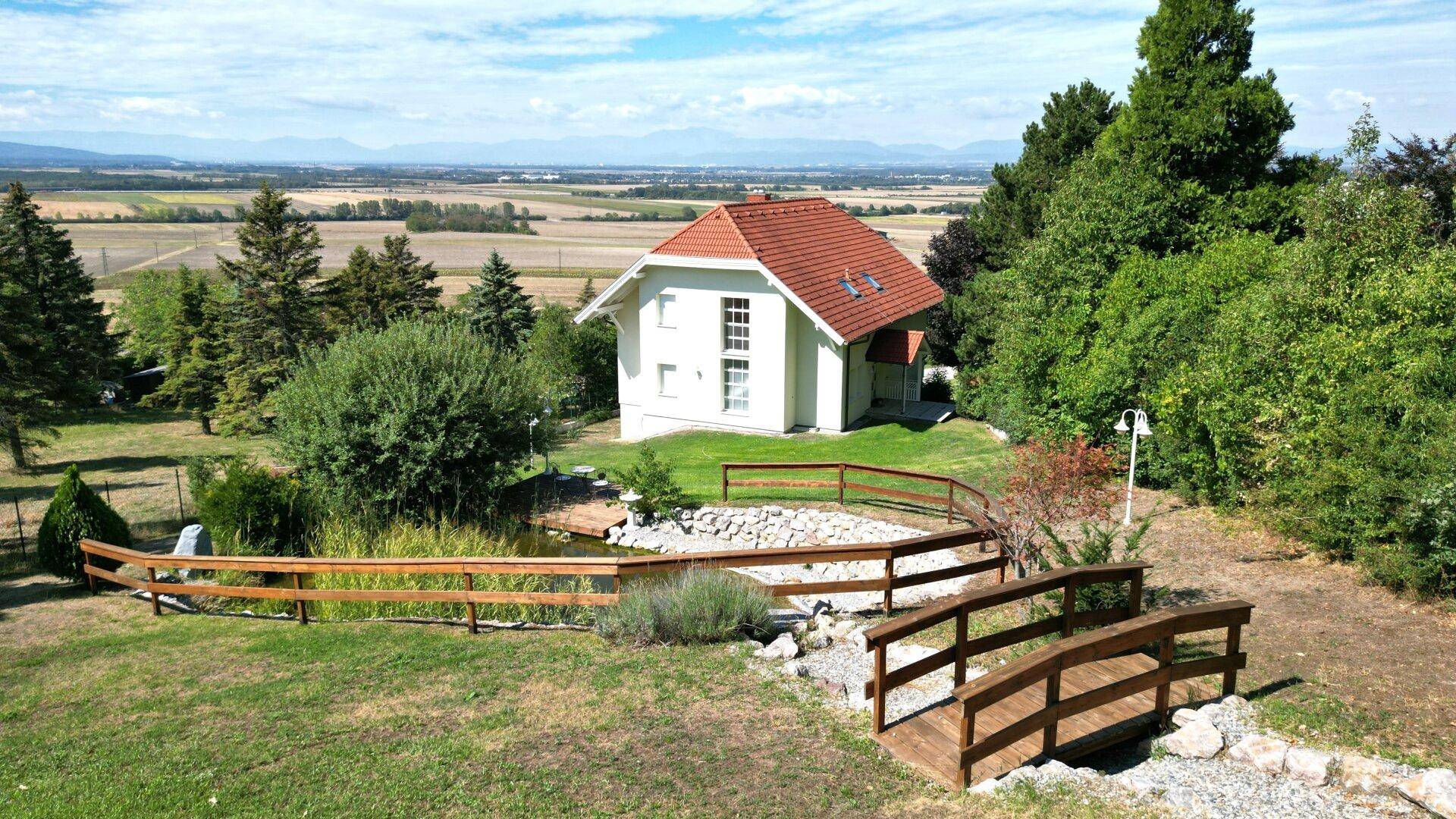 Charmantes Haus mit weitläufigem Garten, Teich und kleiner Holzbrücke, eingebettet in die Natur.