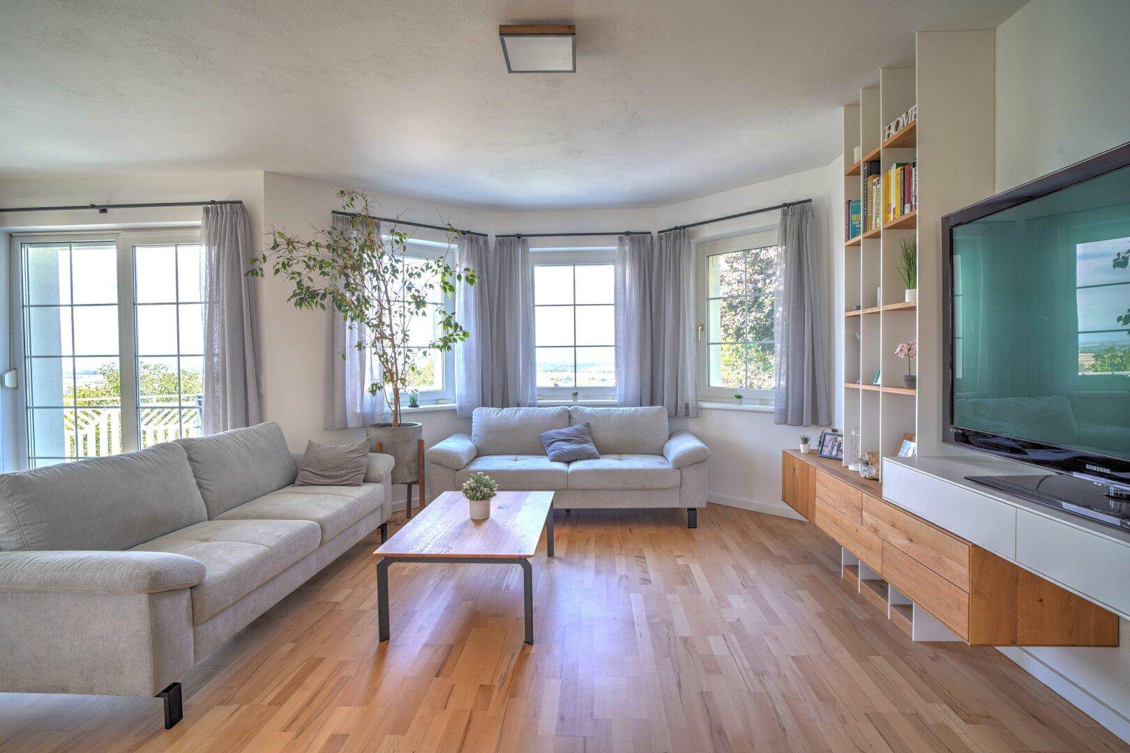 Gemütliches Wohnzimmer mit Holzboden, bequemen Sofas und Blick ins Grüne durch große Fenster.