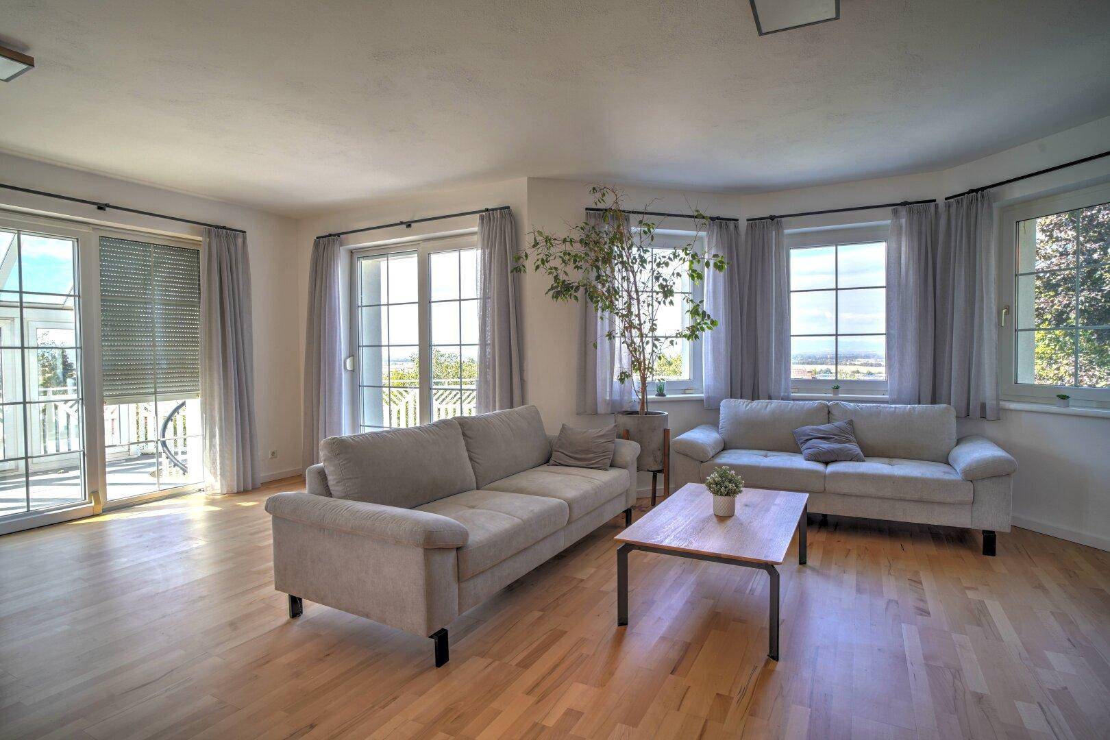 Helles Wohnzimmer mit Zugang zum Balkon, Holzboden und bequemen Sitzgelegenheiten.