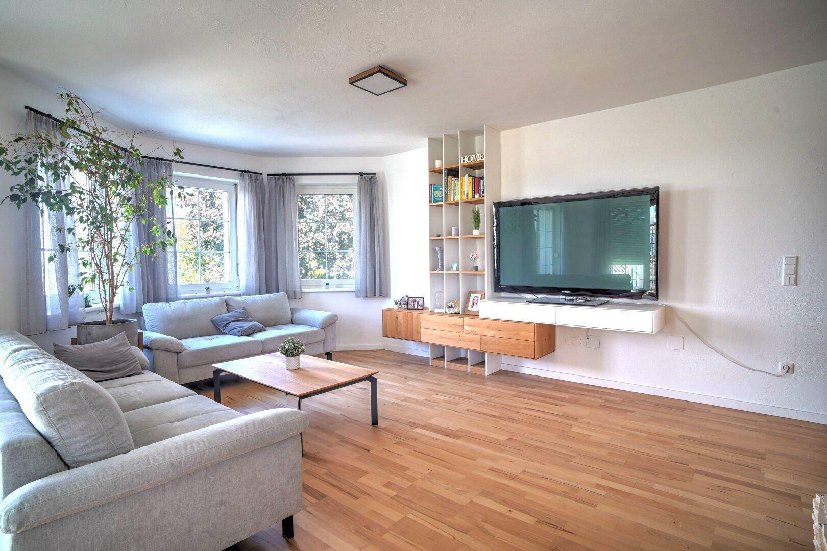 Modern eingerichtetes Wohnzimmer mit Holzboden, TV-Möbel und viel Tageslicht.