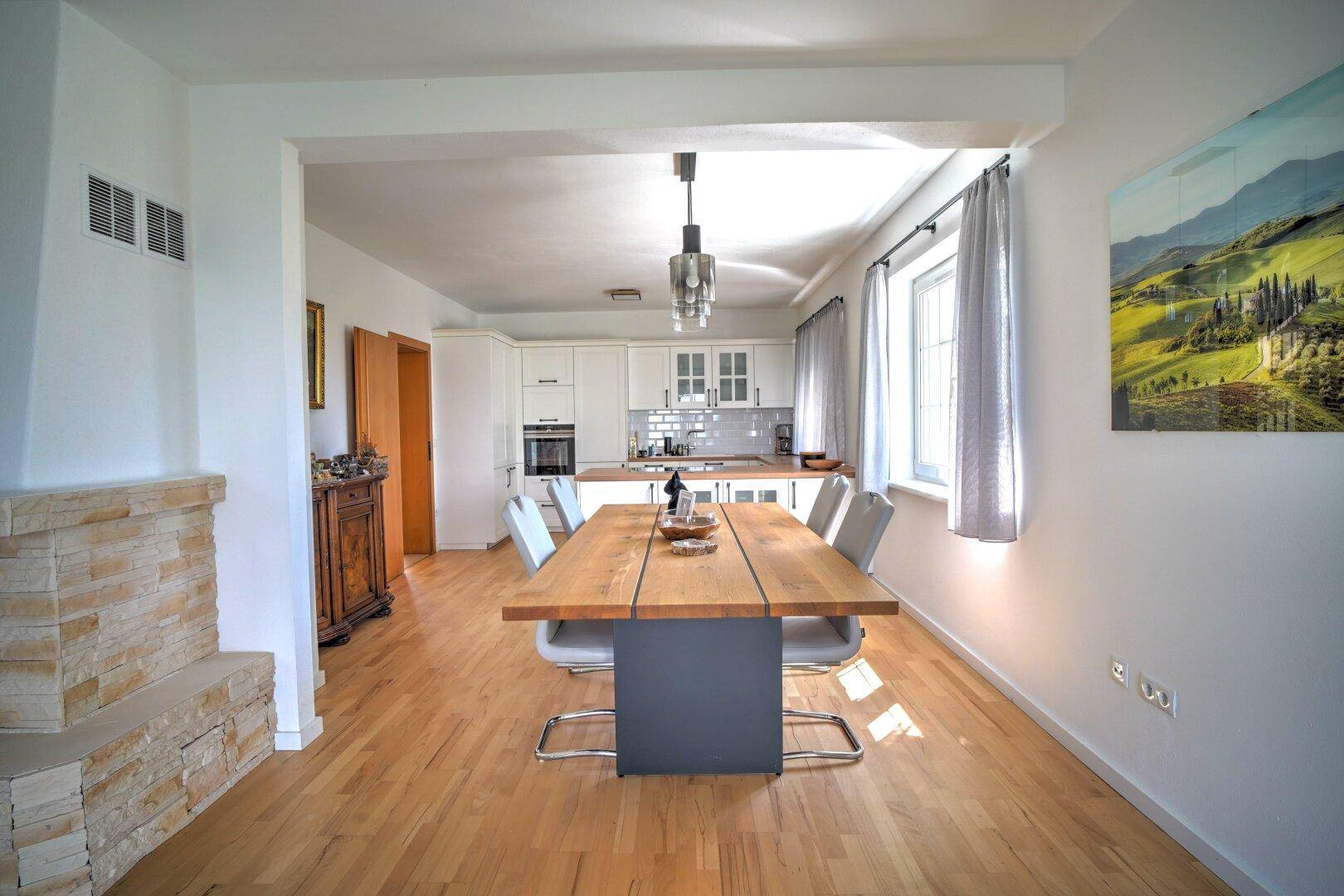 Heller Essbereich mit großem Holztisch und moderner offener Küche im Hintergrund.