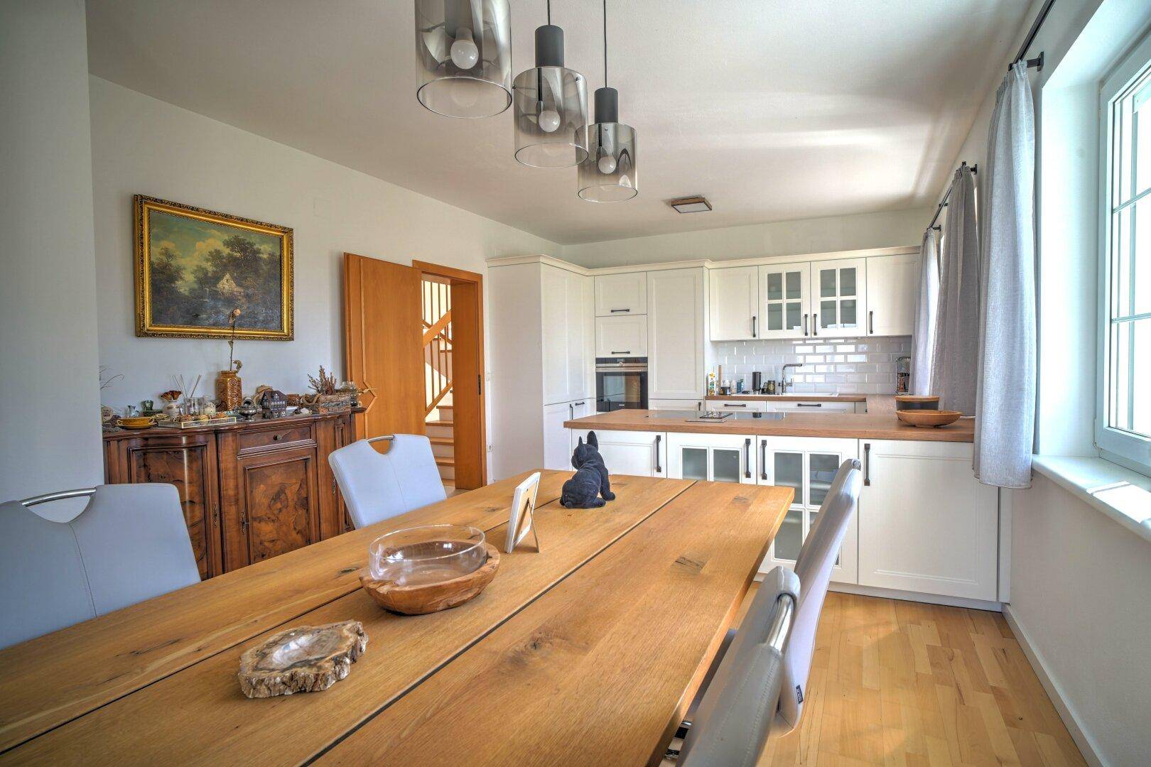 Einladender Essbereich mit Holztisch und Blick auf die moderne Küche und Fenster.