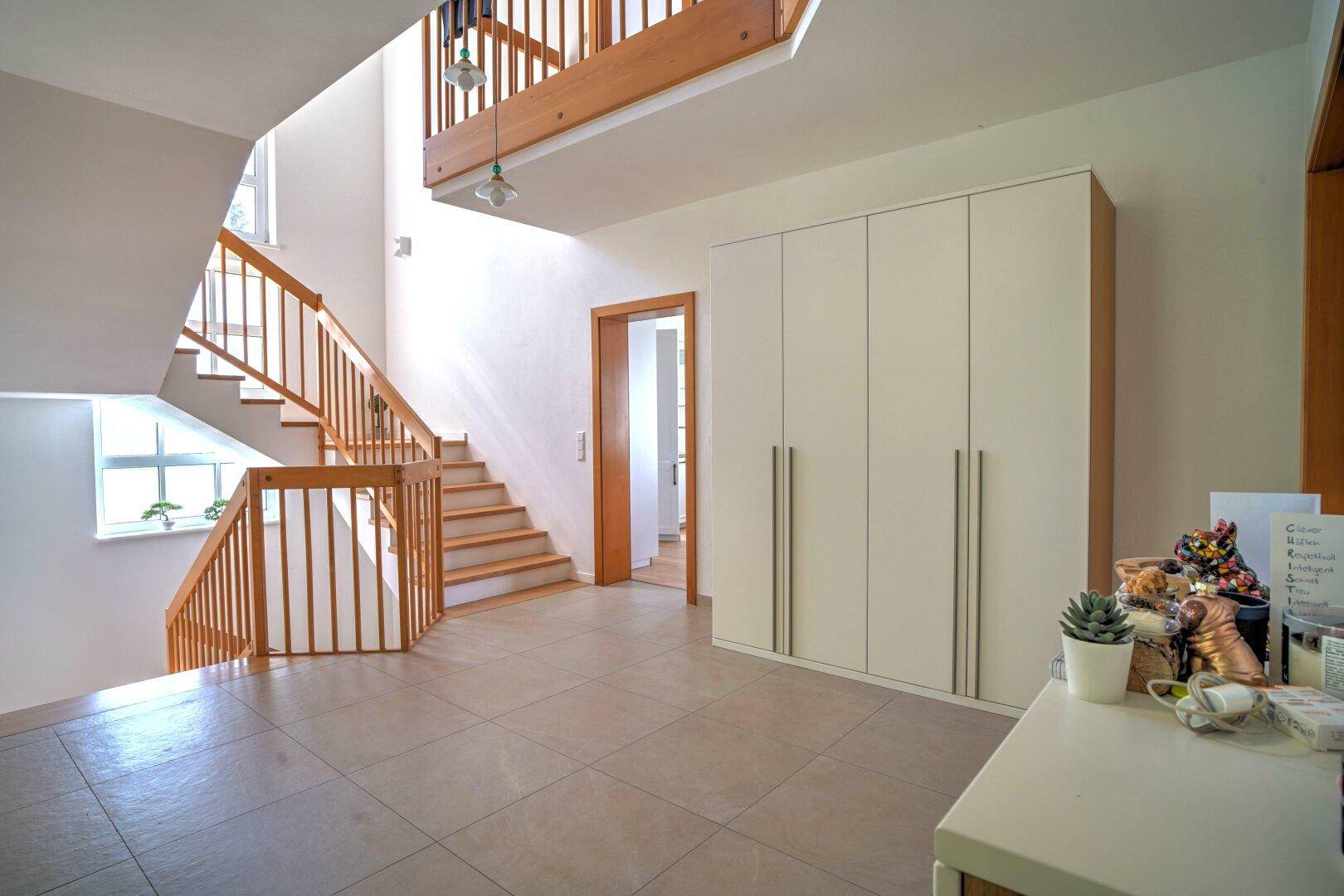 Heller Eingangsbereich mit Holztreppe, Fliesenboden und großem Einbauschrank.
