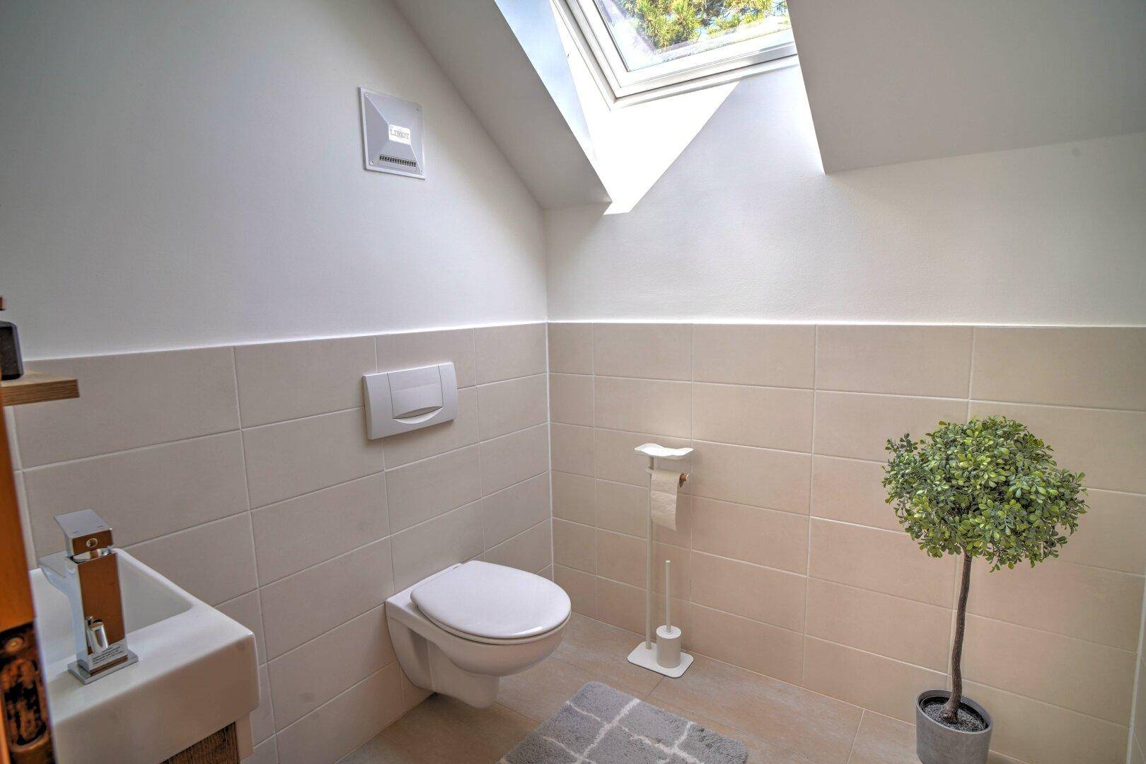 Modernes Gäste-WC unter der Dachschräge mit Wand-WC, Waschbecken und Dachfenster.